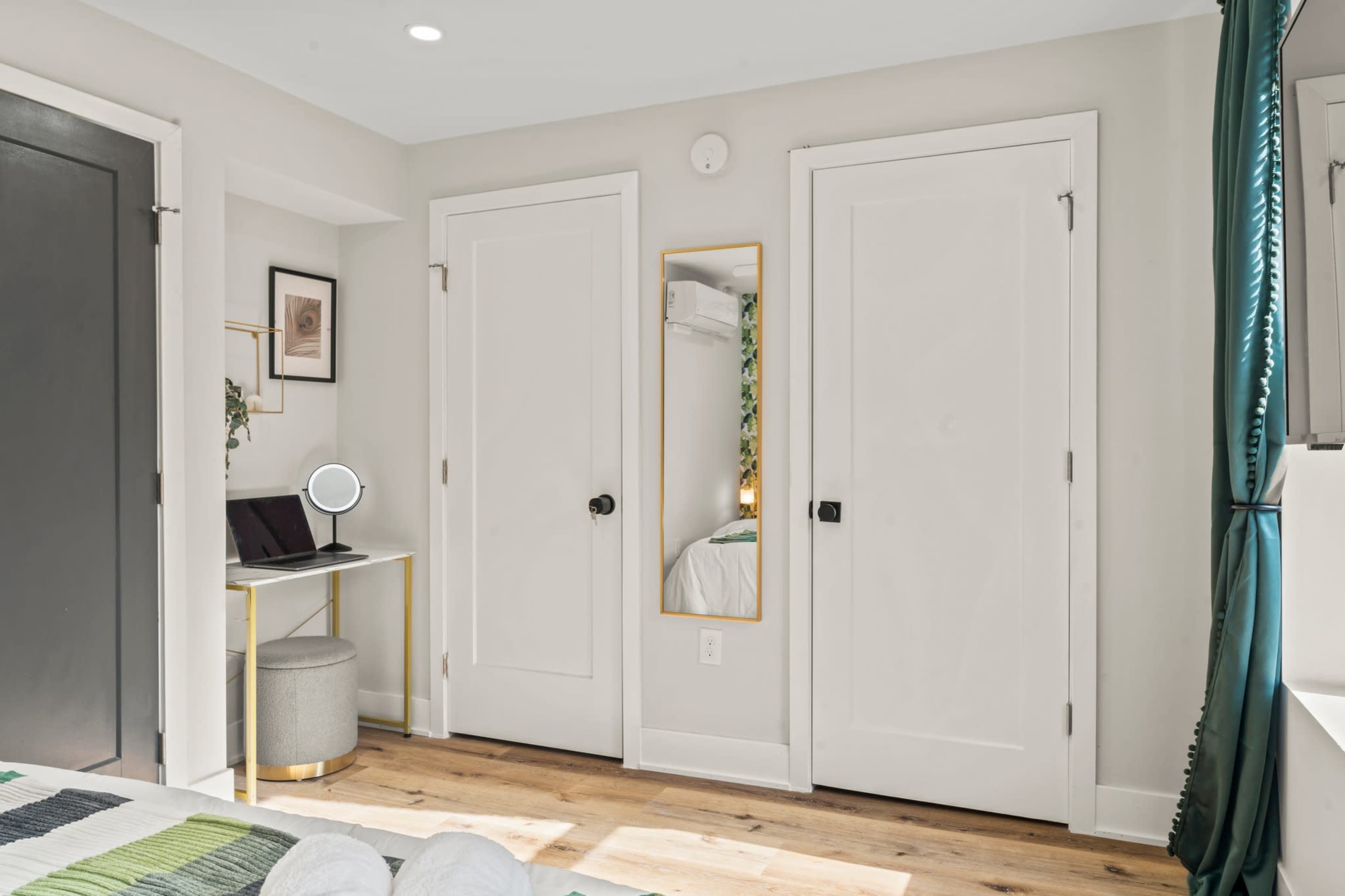 A small room features two white doors, a mirror on the wall, and a desk with a circular mirror and a chair.