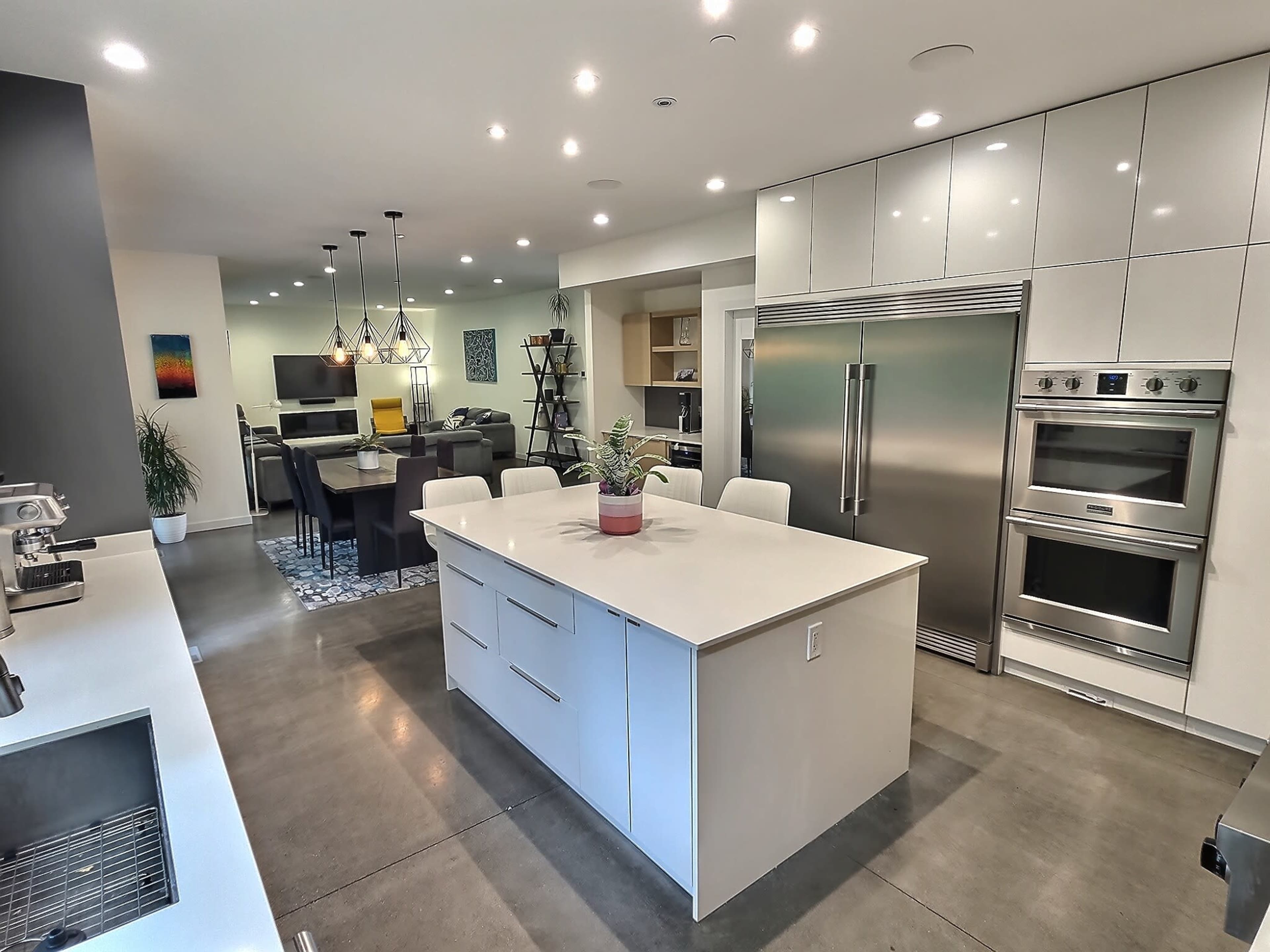 A modern kitchen features a central island with white cabinetry, stainless steel appliances, and a dining area in the background.