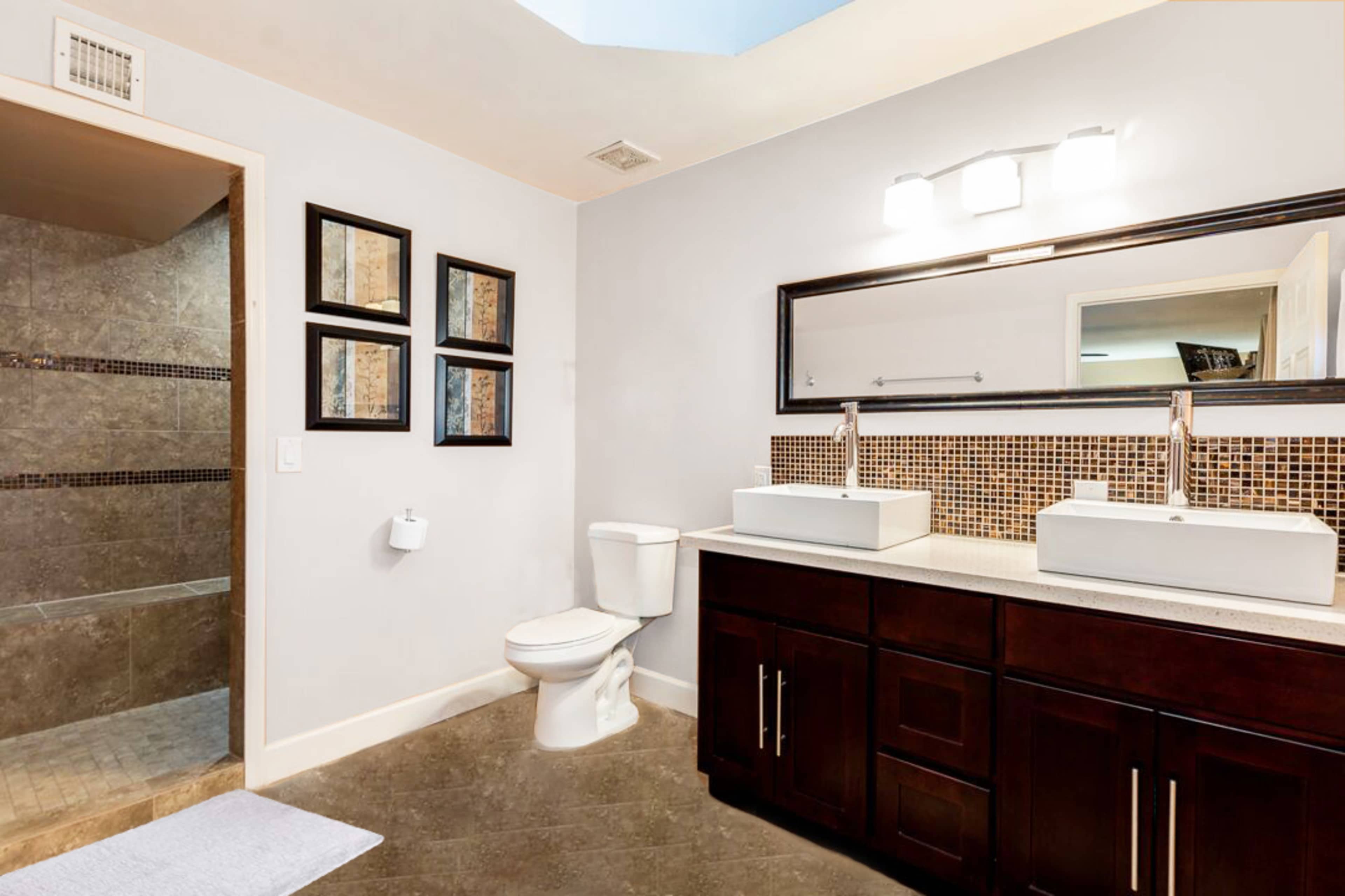 A modern bathroom with dual sinks, a tiled shower area, and dark cabinetry.