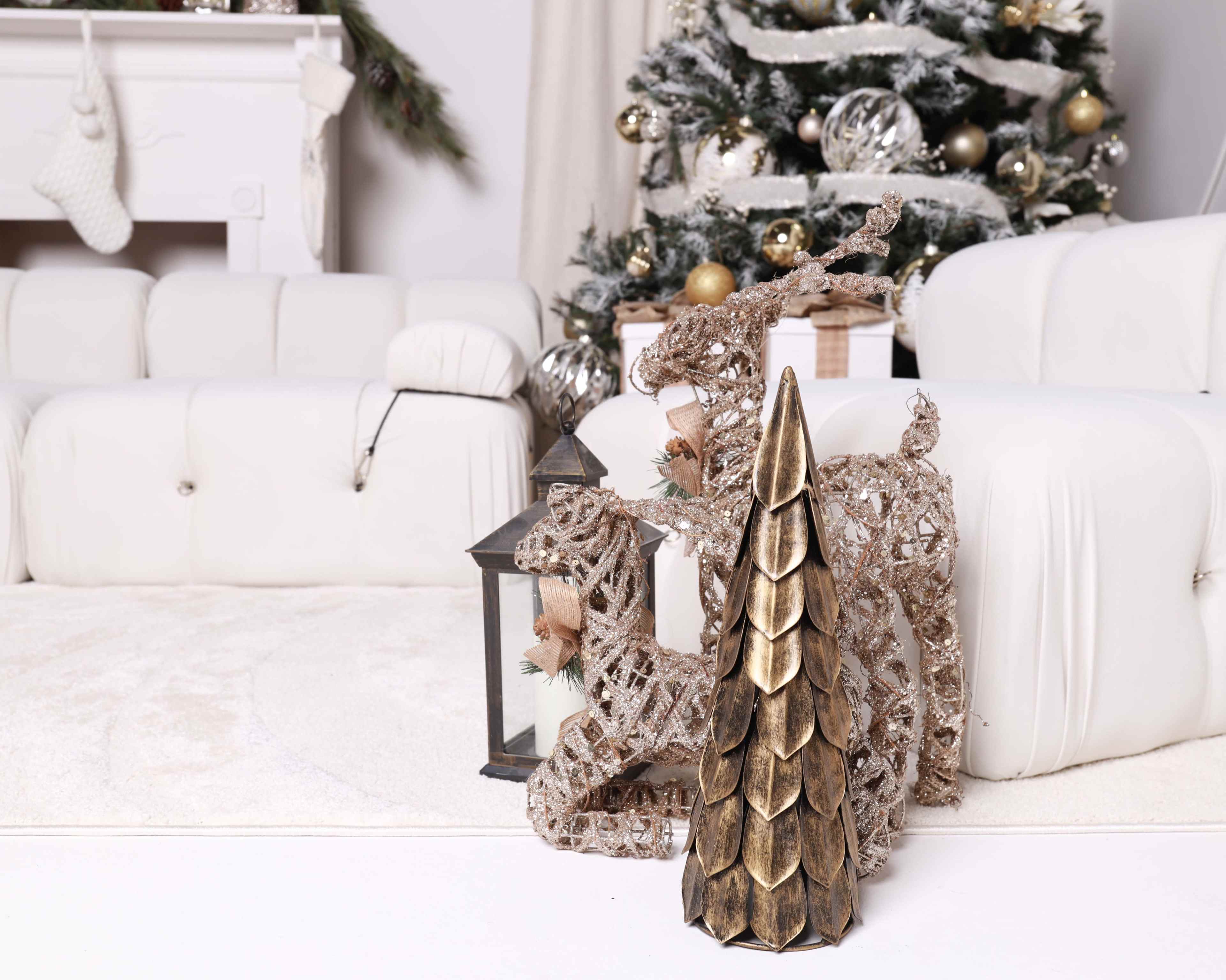 A decorative reindeer and a golden tree stand beside a lantern in a cozy living room adorned for the holidays.