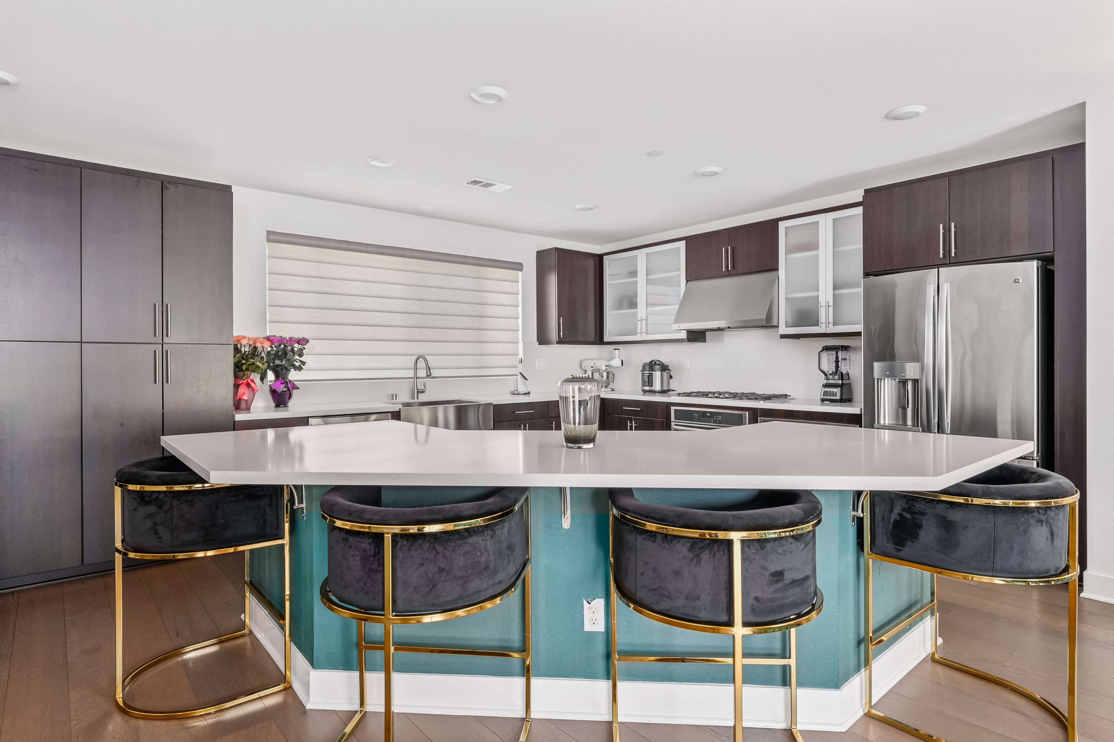 A modern kitchen features dark cabinetry, stainless steel appliances, and a large island with circular bar stools.
