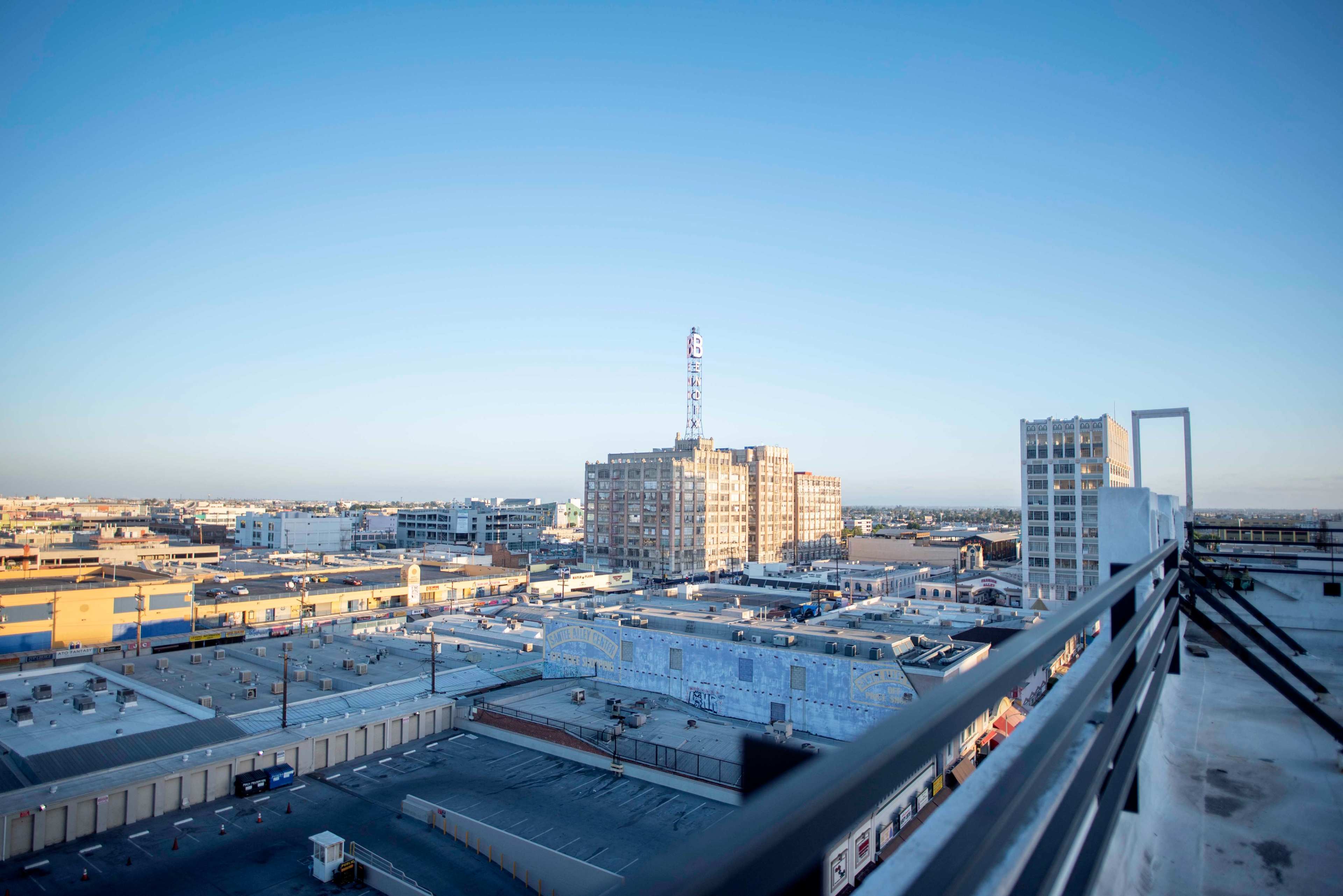 The image shows a panoramic view of a city skyline with low-rise buildings, a mural-covered structure, and a broadcasting tower in the distance.