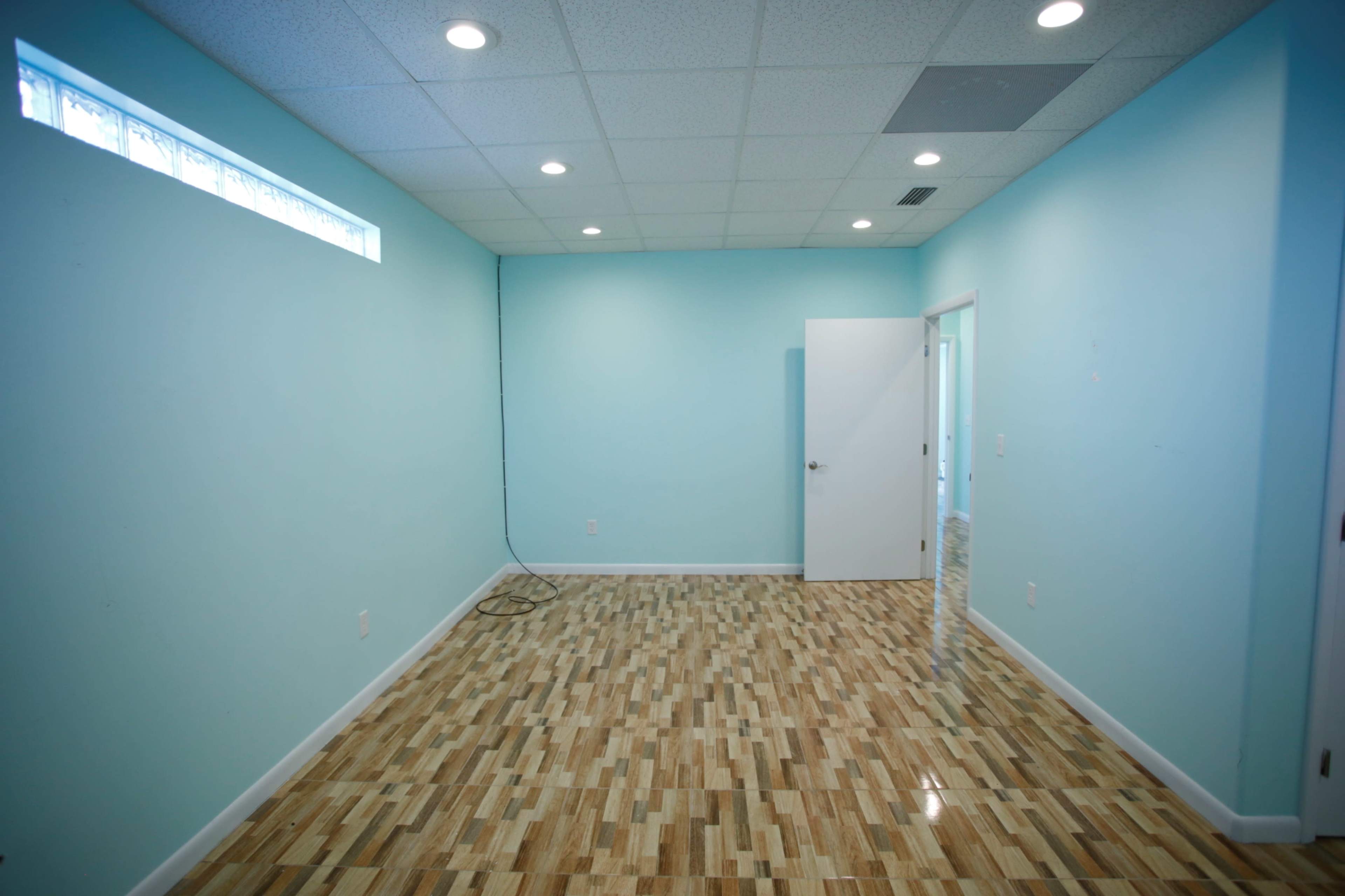 The image shows an empty room with light blue walls, a wooden floor, and a single door leading to another area.