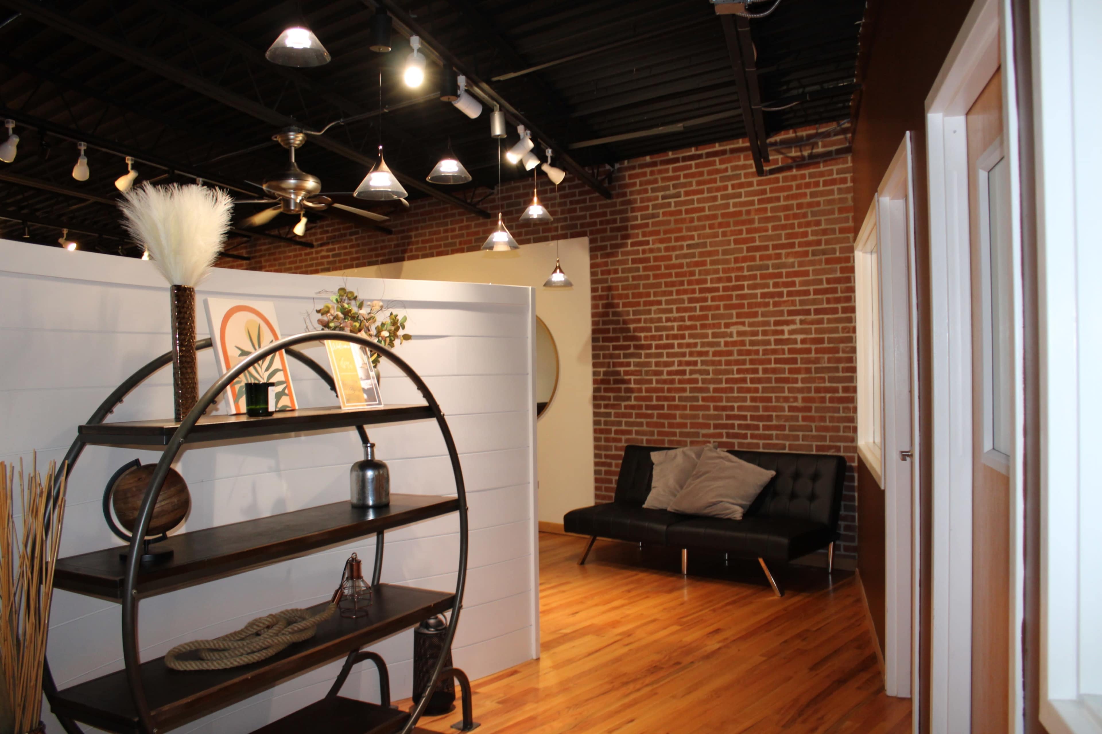 A modern interior space featuring a black sofa, a circular shelf with decorative items, and exposed brick walls.