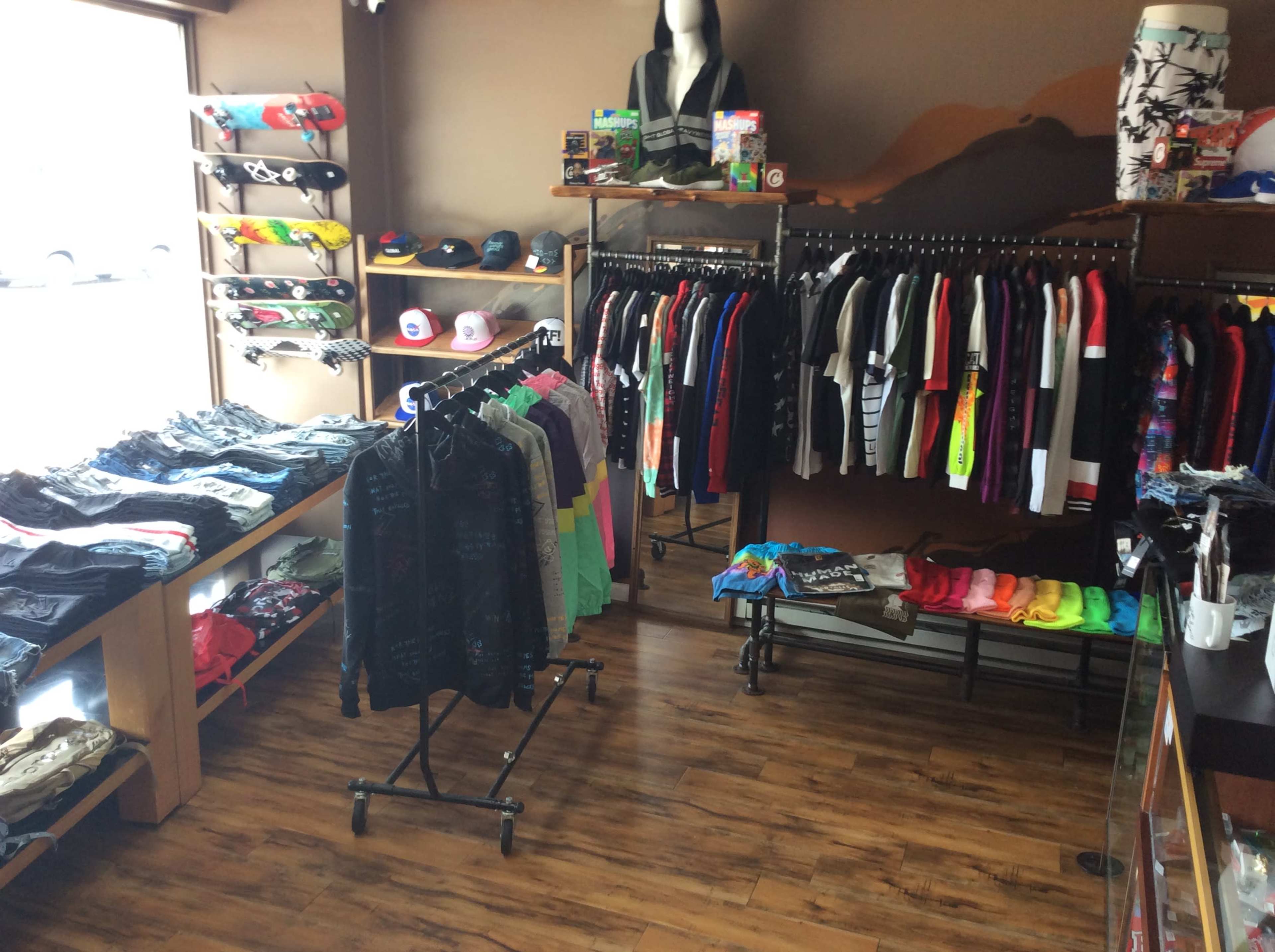 The image shows a clothing store interior with clothes displayed on racks and shelves, featuring various apparel including shirts, shorts, and hats.