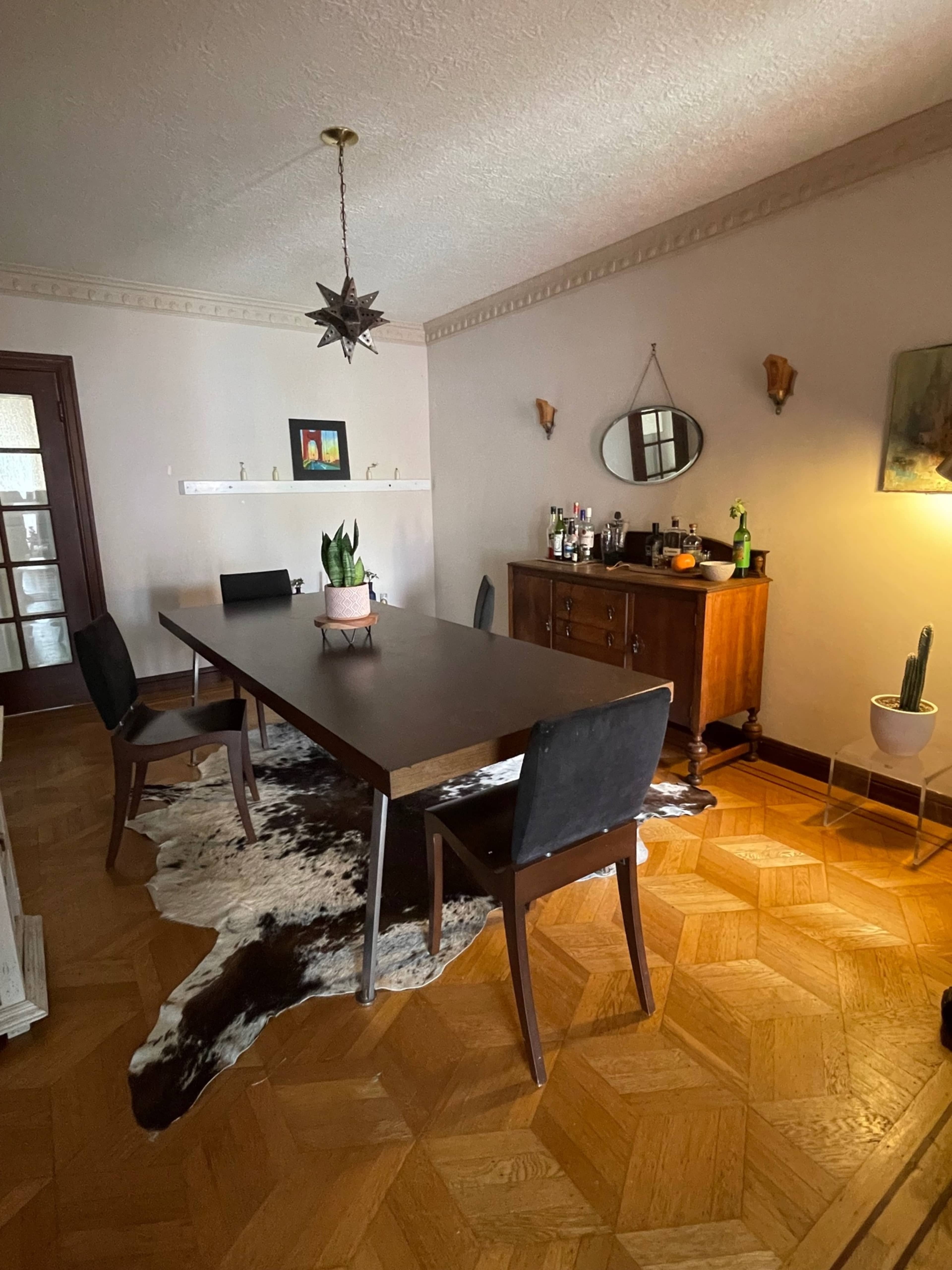A spacious dining area features a long table, black chairs, a wooden sideboard, and decorative wall accents.