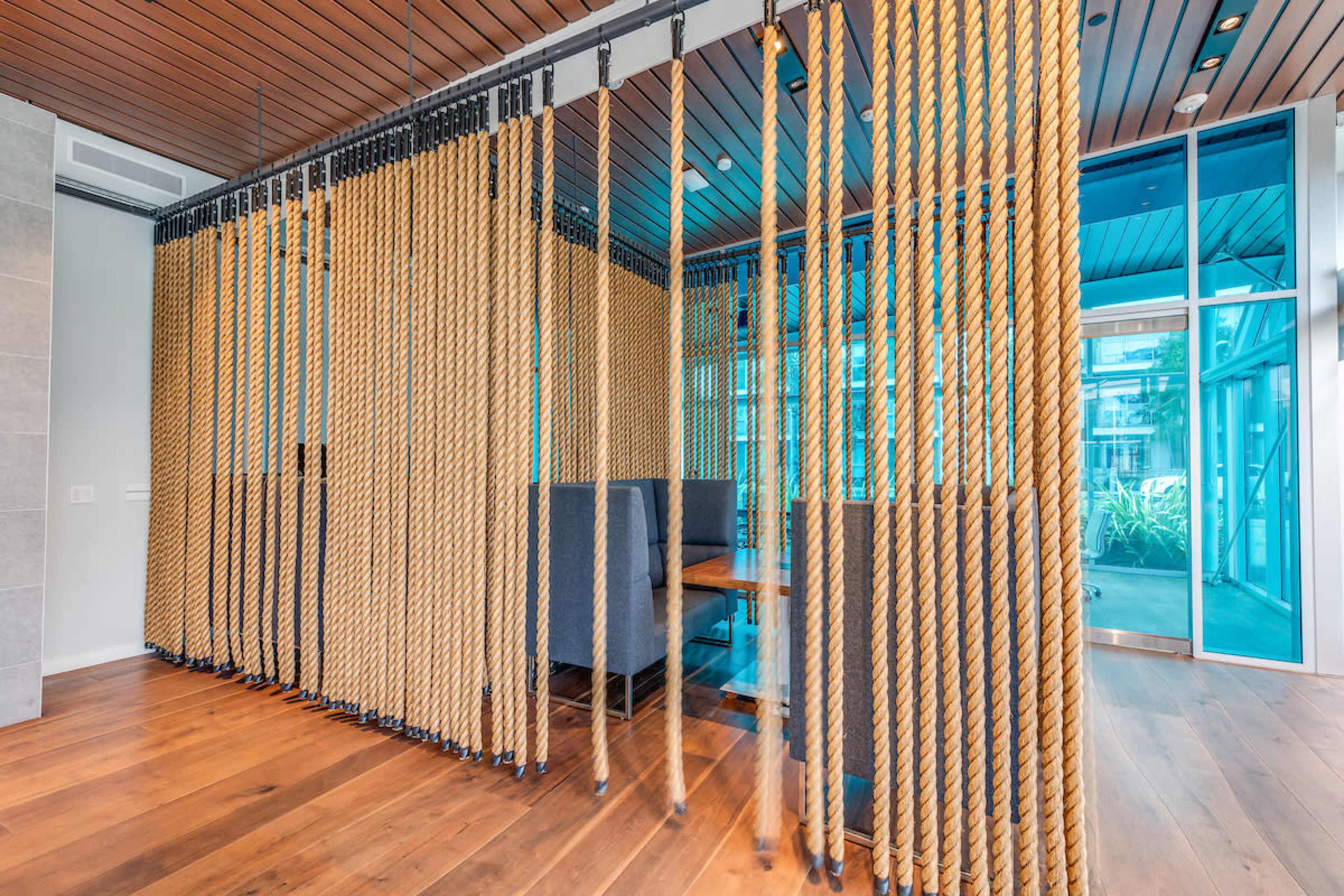 A modern interior space featuring a rope curtain that divides a seated area with a wooden table and chairs from the surrounding environment.