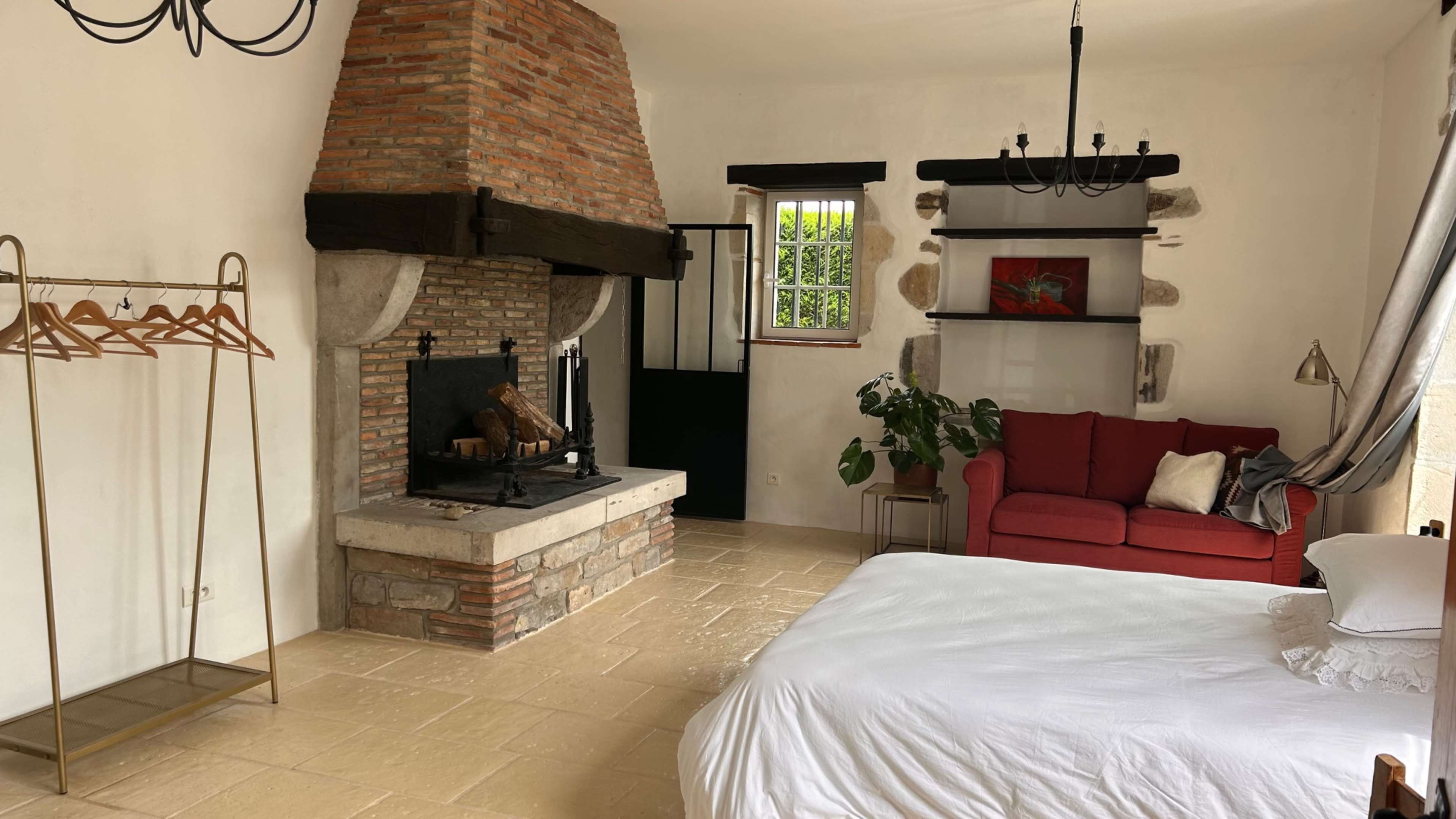 A spacious room with a large bed, a red couch, a stone fireplace with a brick chimney, and a clothing rack.