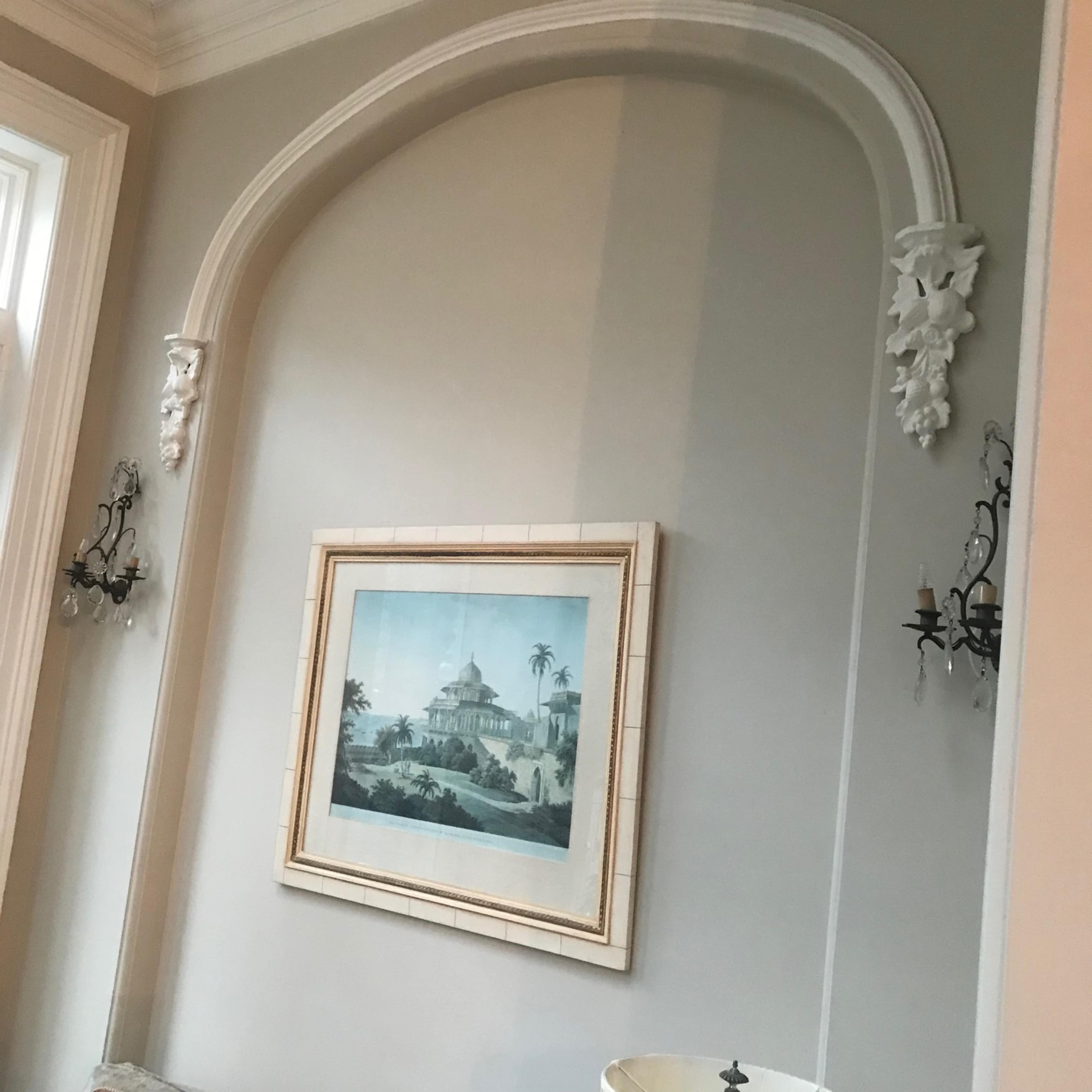 A wall with an arched niche that holds a framed artwork, flanked by two wall sconces.