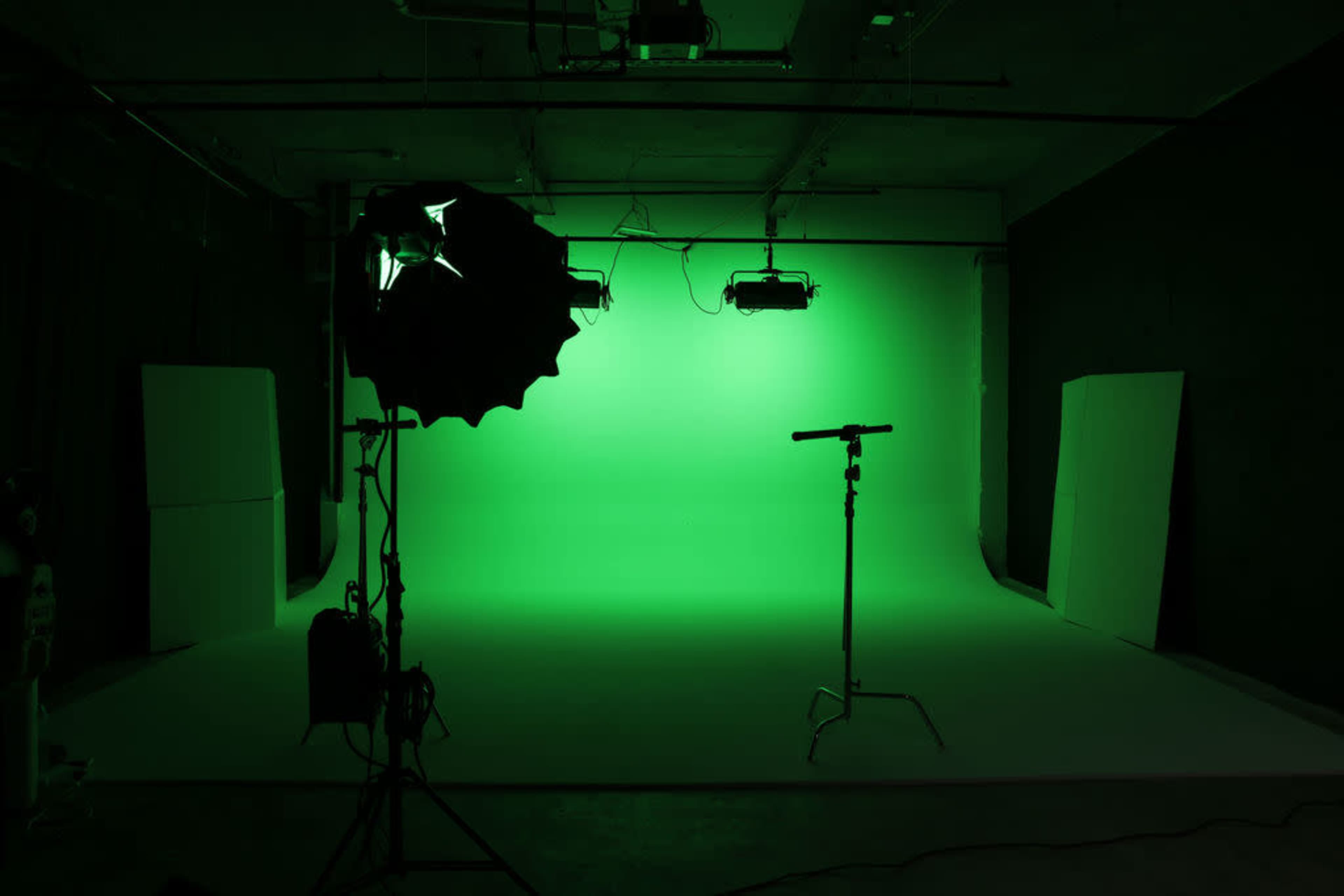 The image shows a photography studio with a green backdrop, a light source, and a stand in the foreground.