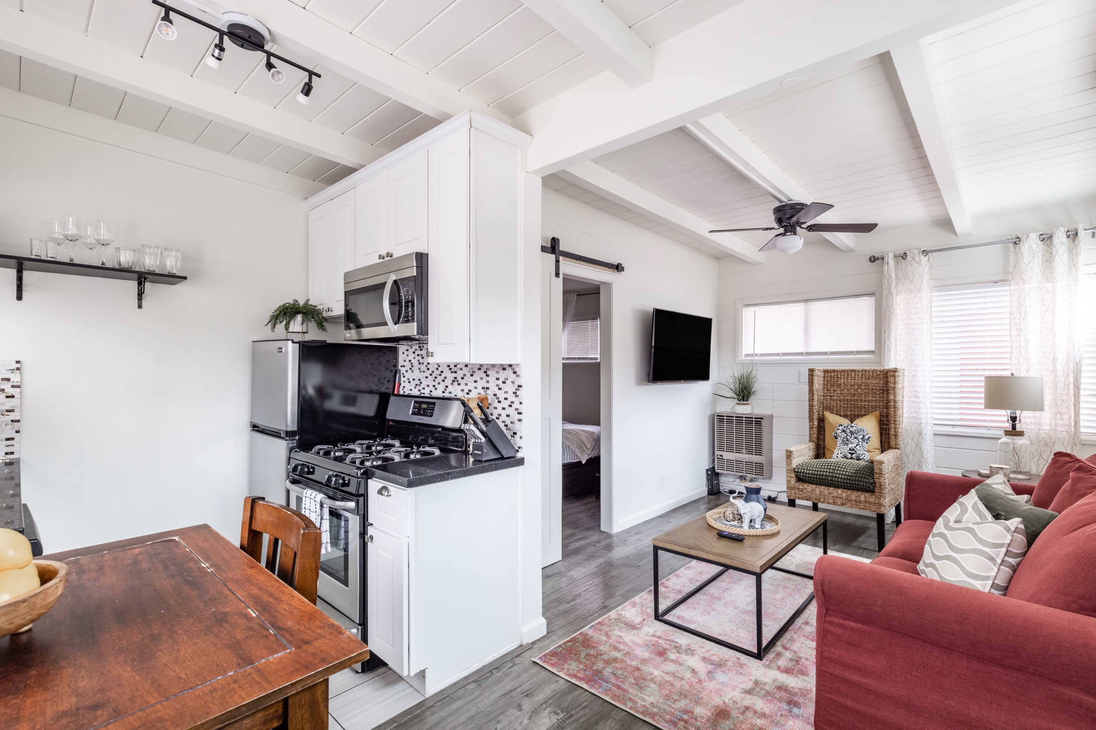 A small, open-concept living space with a kitchen, dining area, and seating area featuring a red couch and wooden dining table.