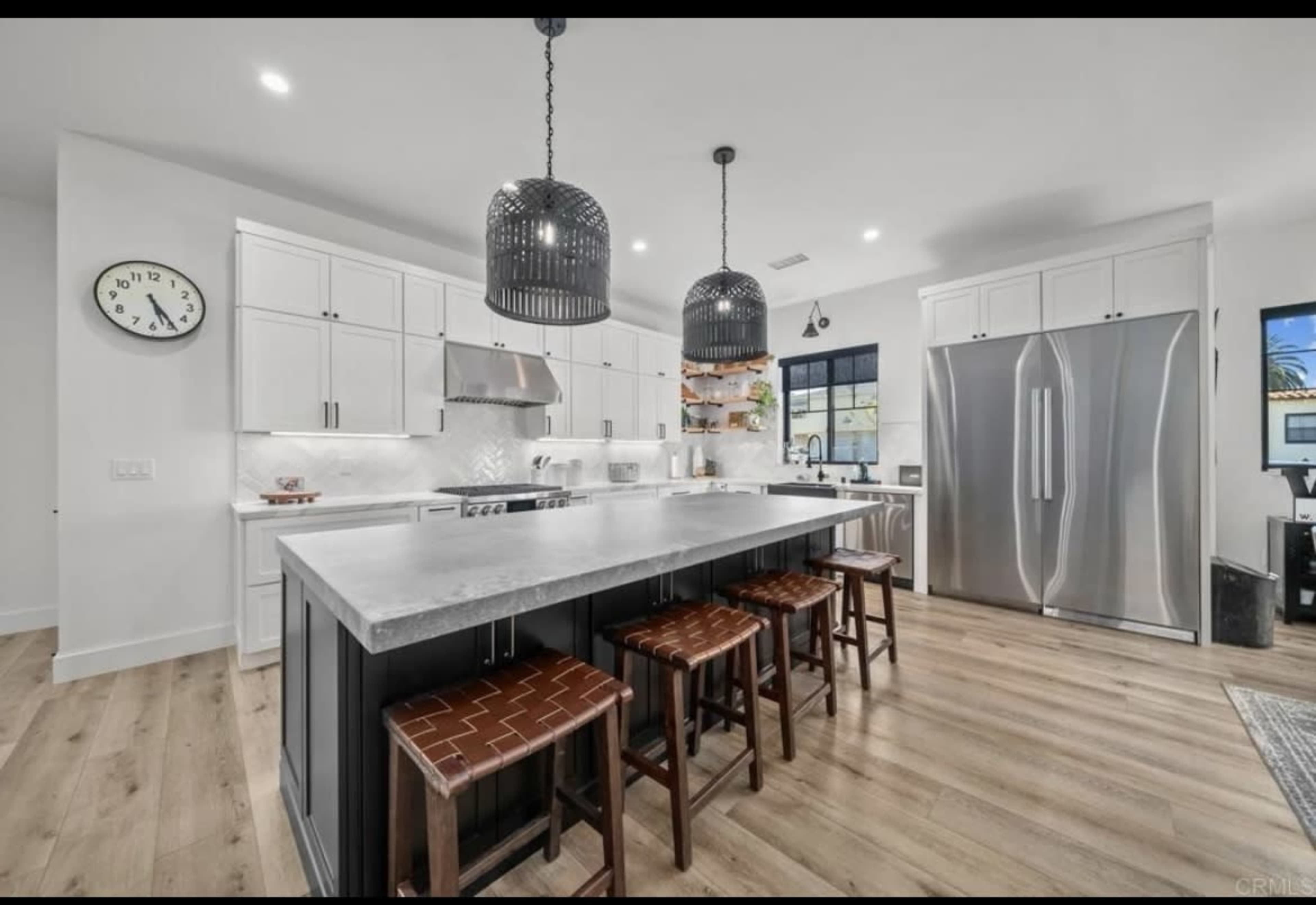 The image shows a modern kitchen with white cabinetry, a large island with bar stools, stainless steel appliances, and a minimalist design.