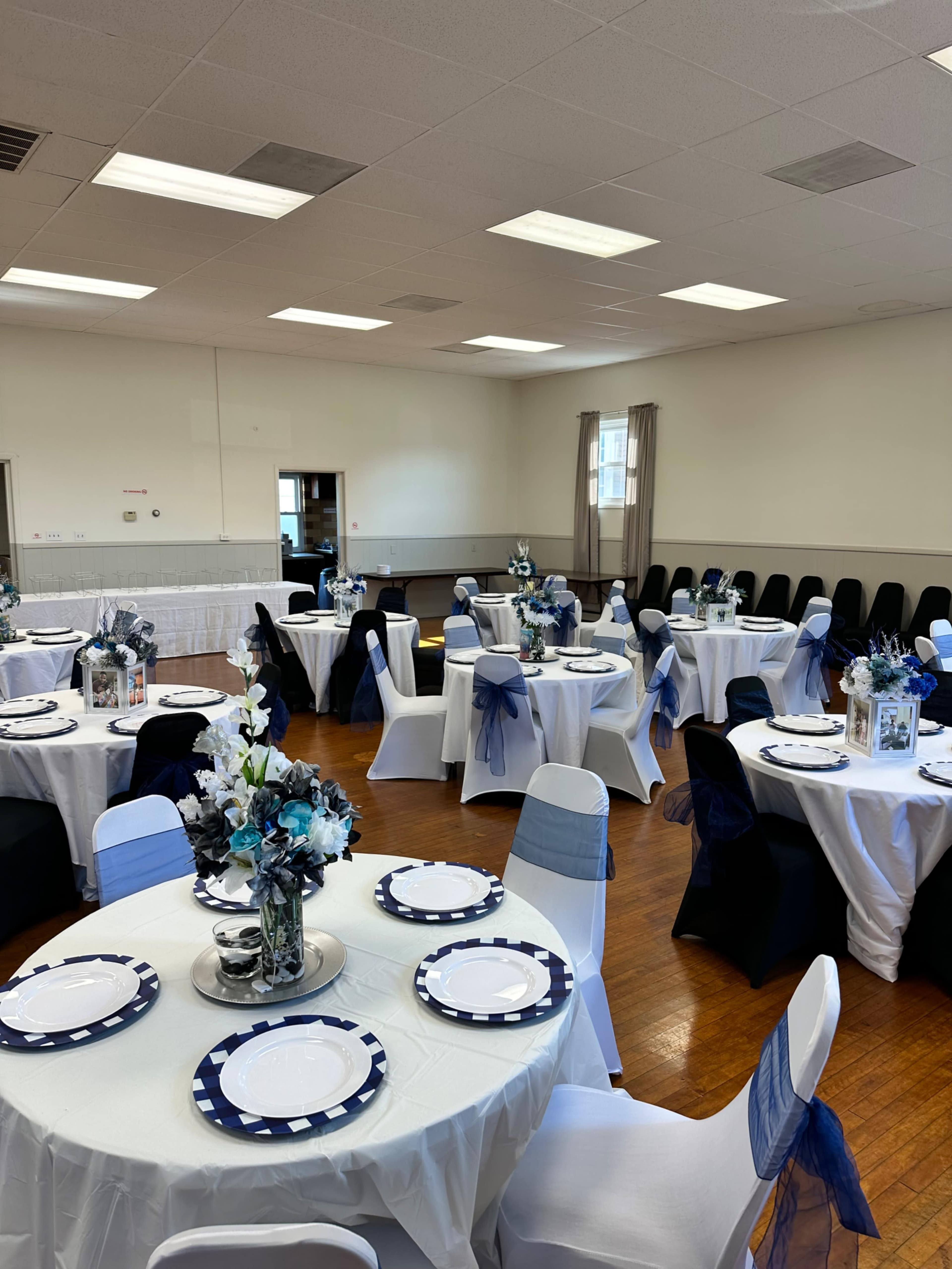 The image shows a well-arranged event space with round tables covered in white tablecloths and navy blue accents, surrounded by matching chairs.