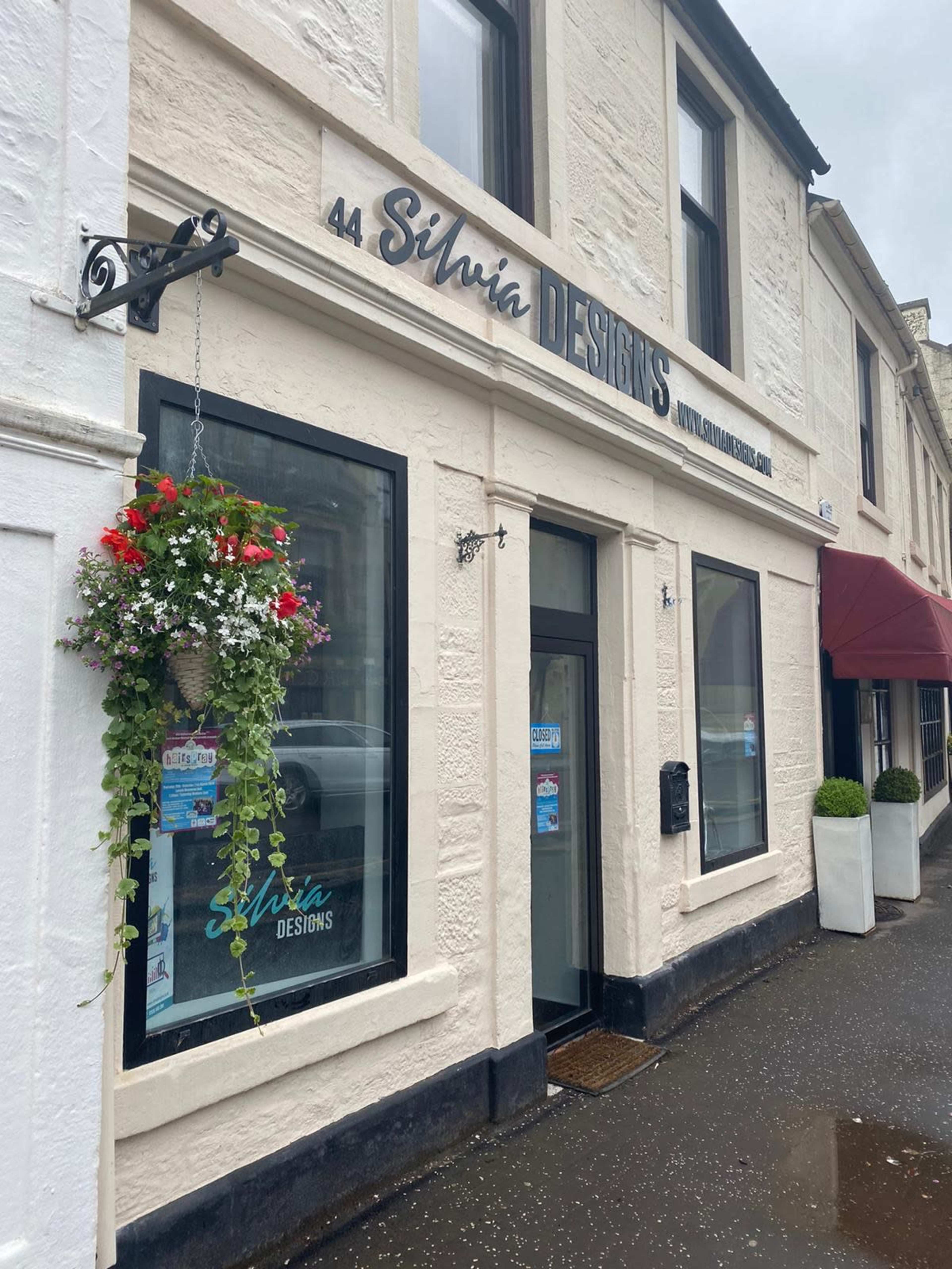 The storefront of Silvia Designs, located at 44, features a sign above the entrance and hanging flower baskets.