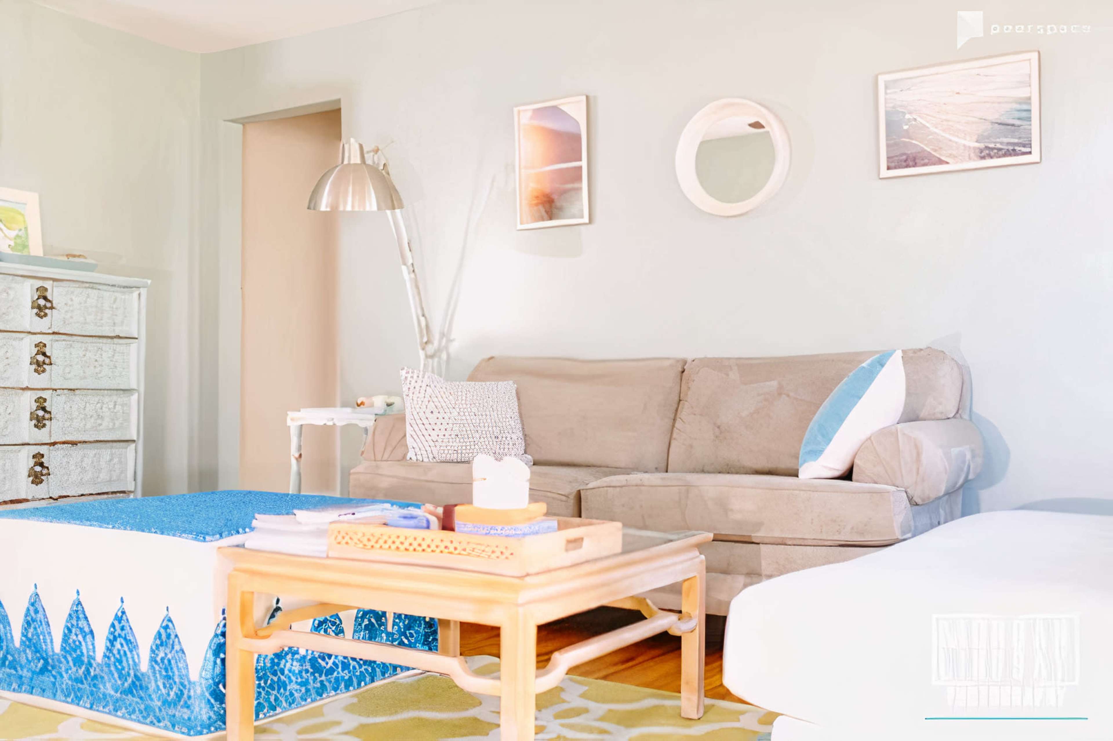 A light and airy living room features a beige sofa, a blue-patterned coffee table, and a decorative side cabinet against a pastel wall.