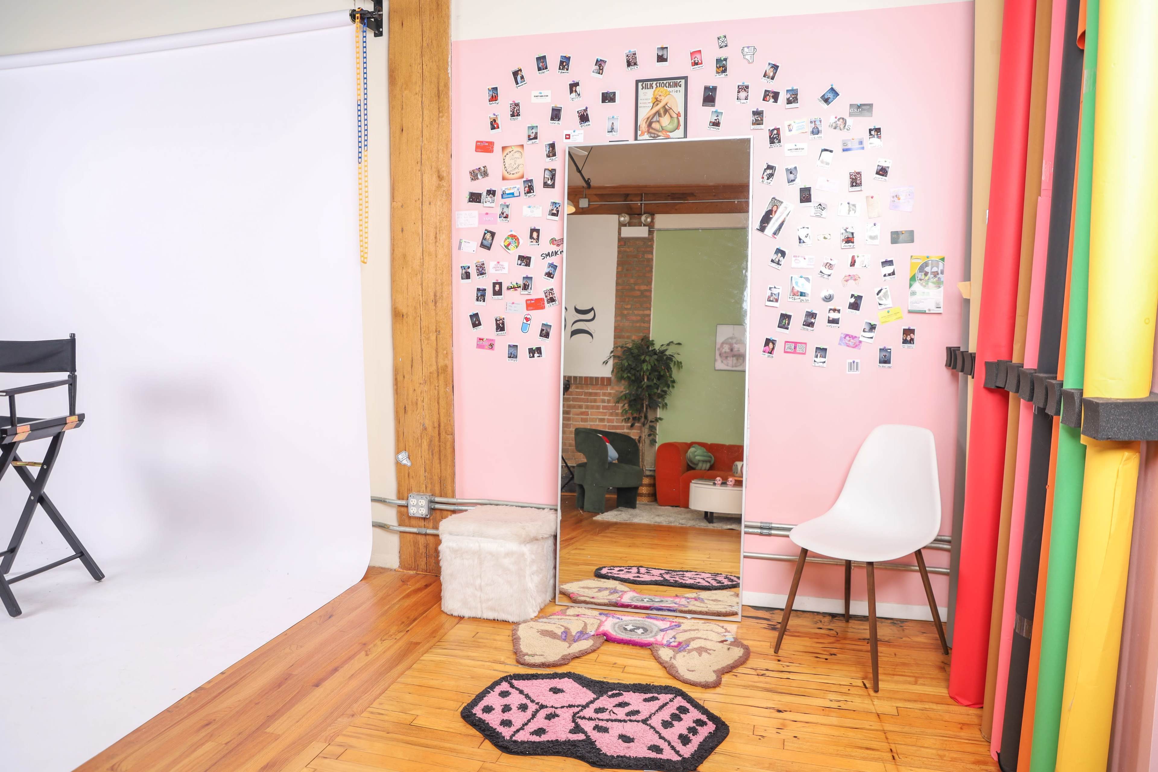The image shows a creative studio space featuring a pink wall adorned with various photographs and a section with a white backdrop for photography.