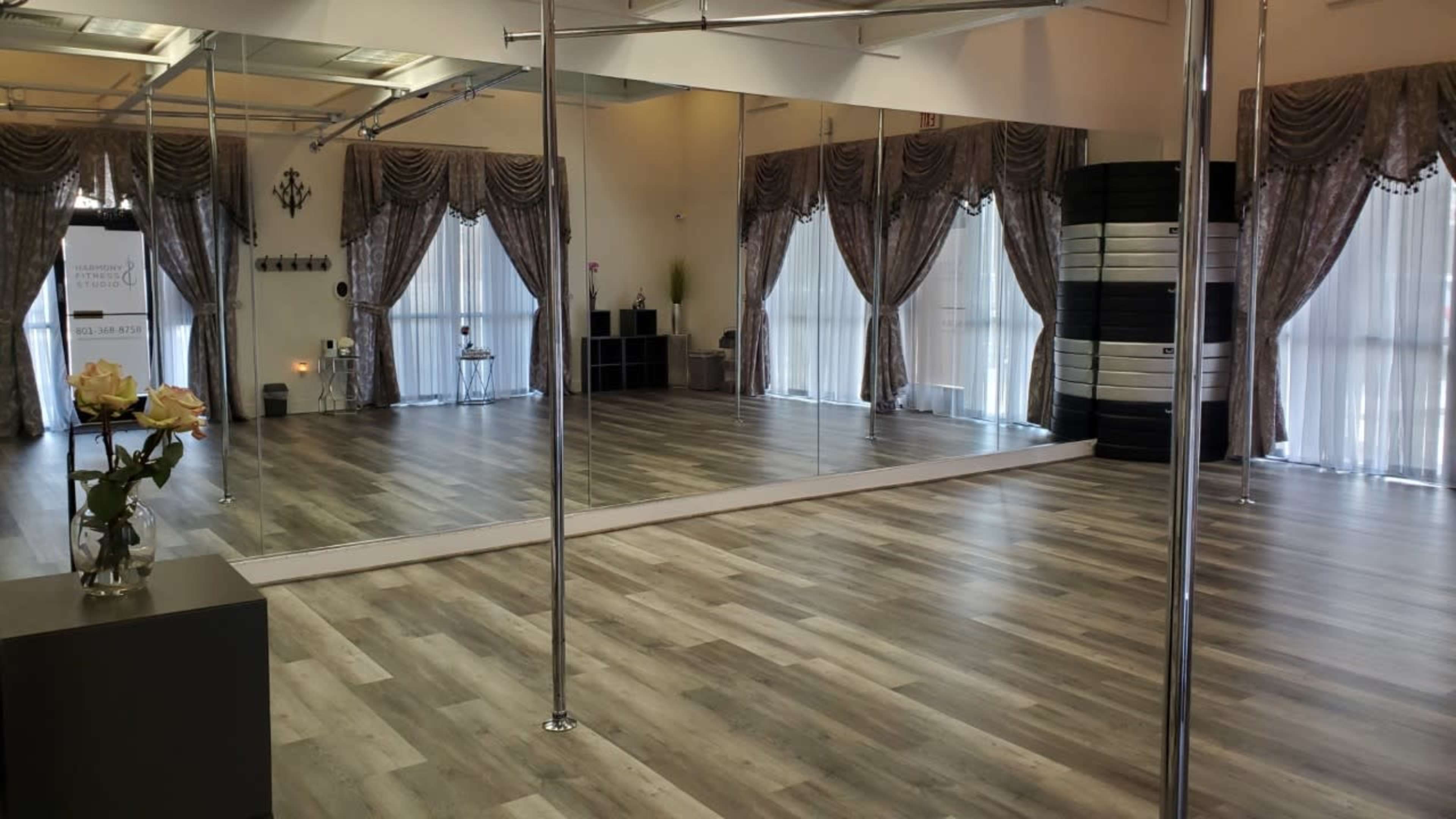 A spacious dance studio with wooden flooring, large mirrors, and sheer curtains framing the windows.
