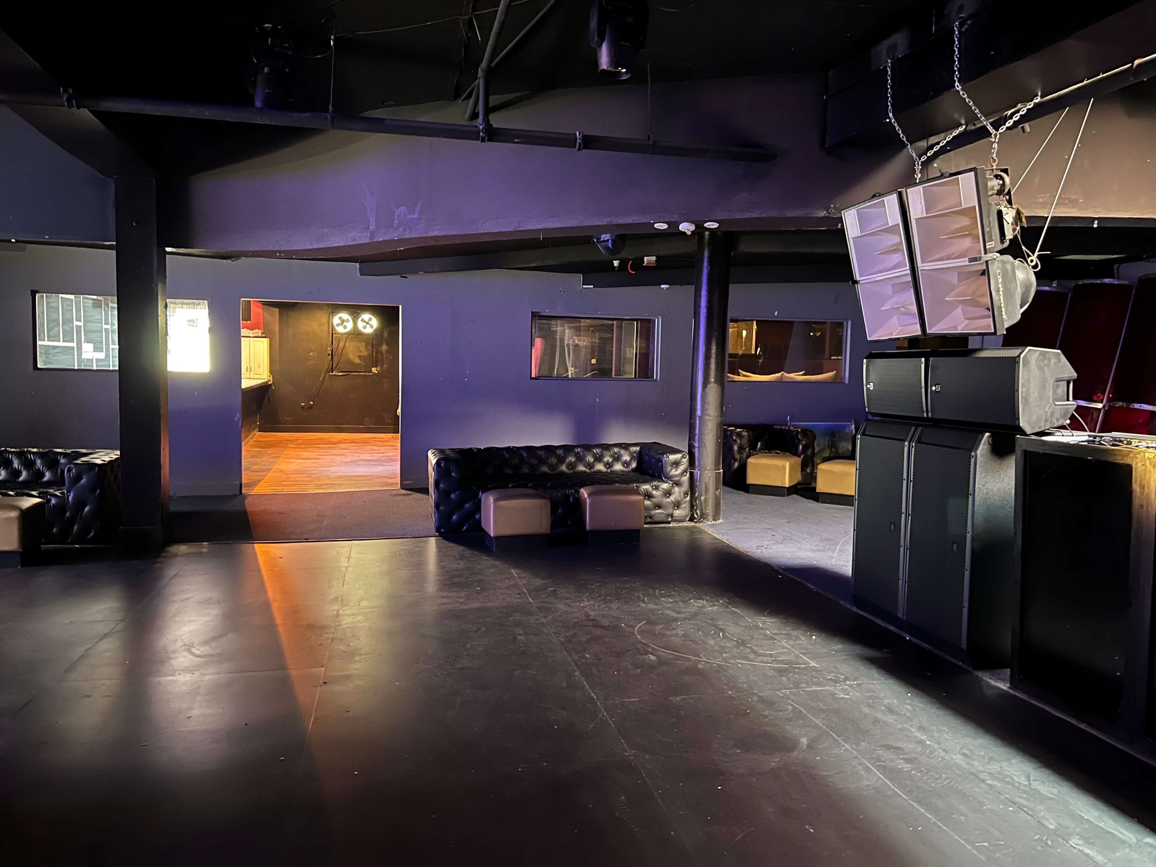 The interior of a dimly lit lounge with black walls, leather seating, and sound equipment visible.