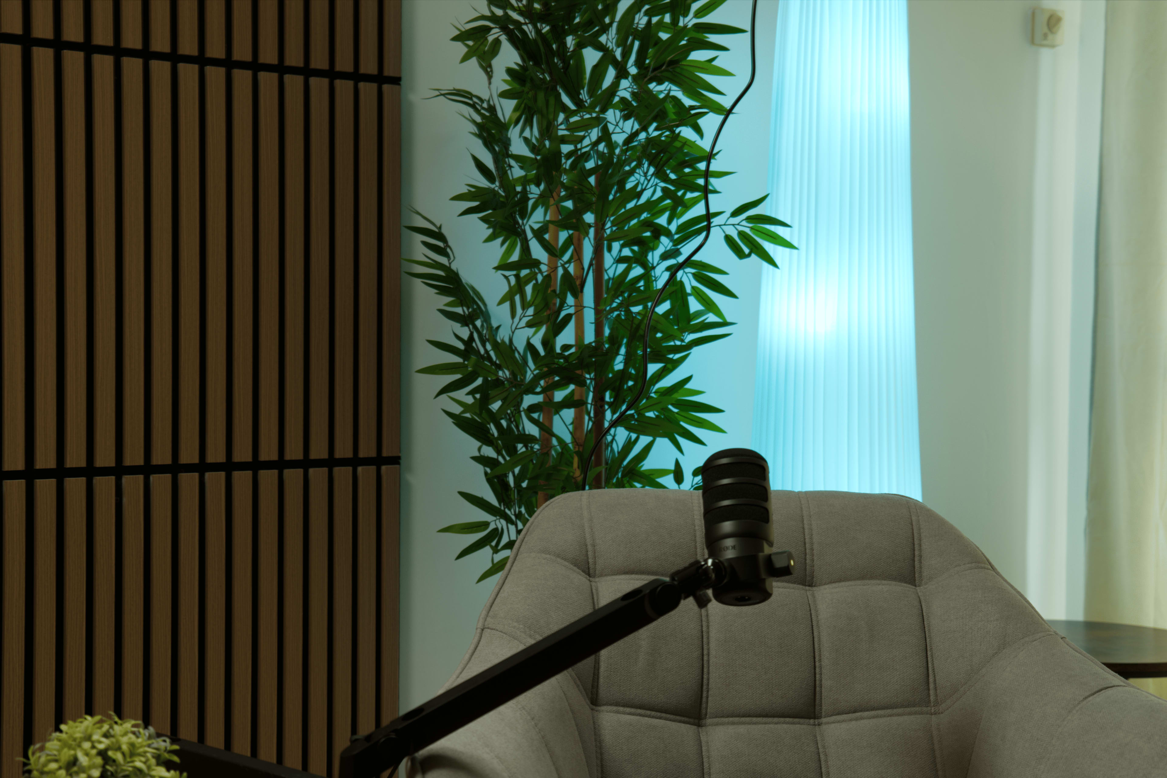 A modern interior features a gray armchair beside a tall plant and a softly lit blue column.