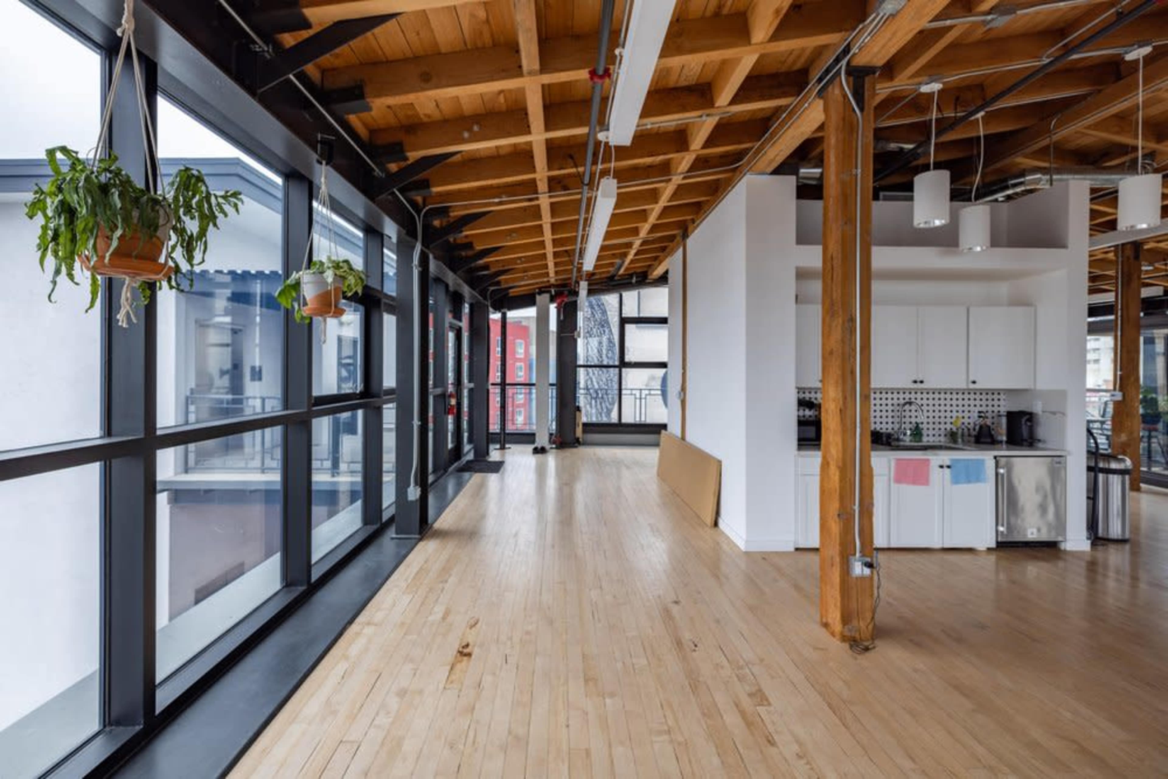 An open-concept interior space with wooden beams, large windows, and a kitchenette at one end.