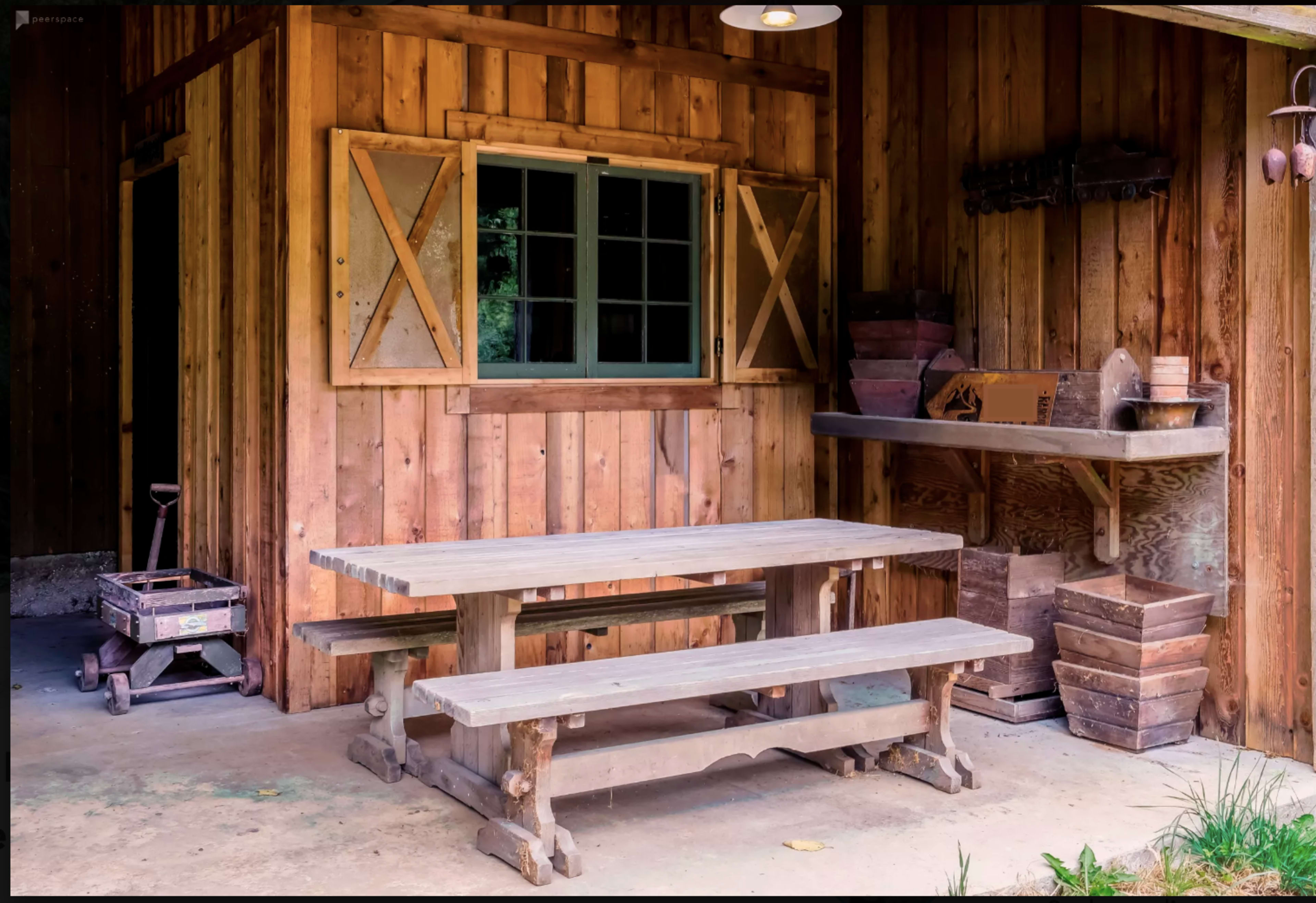 A wooden picnic table in front of a rustic shed with a window and various tools on a workbench.
