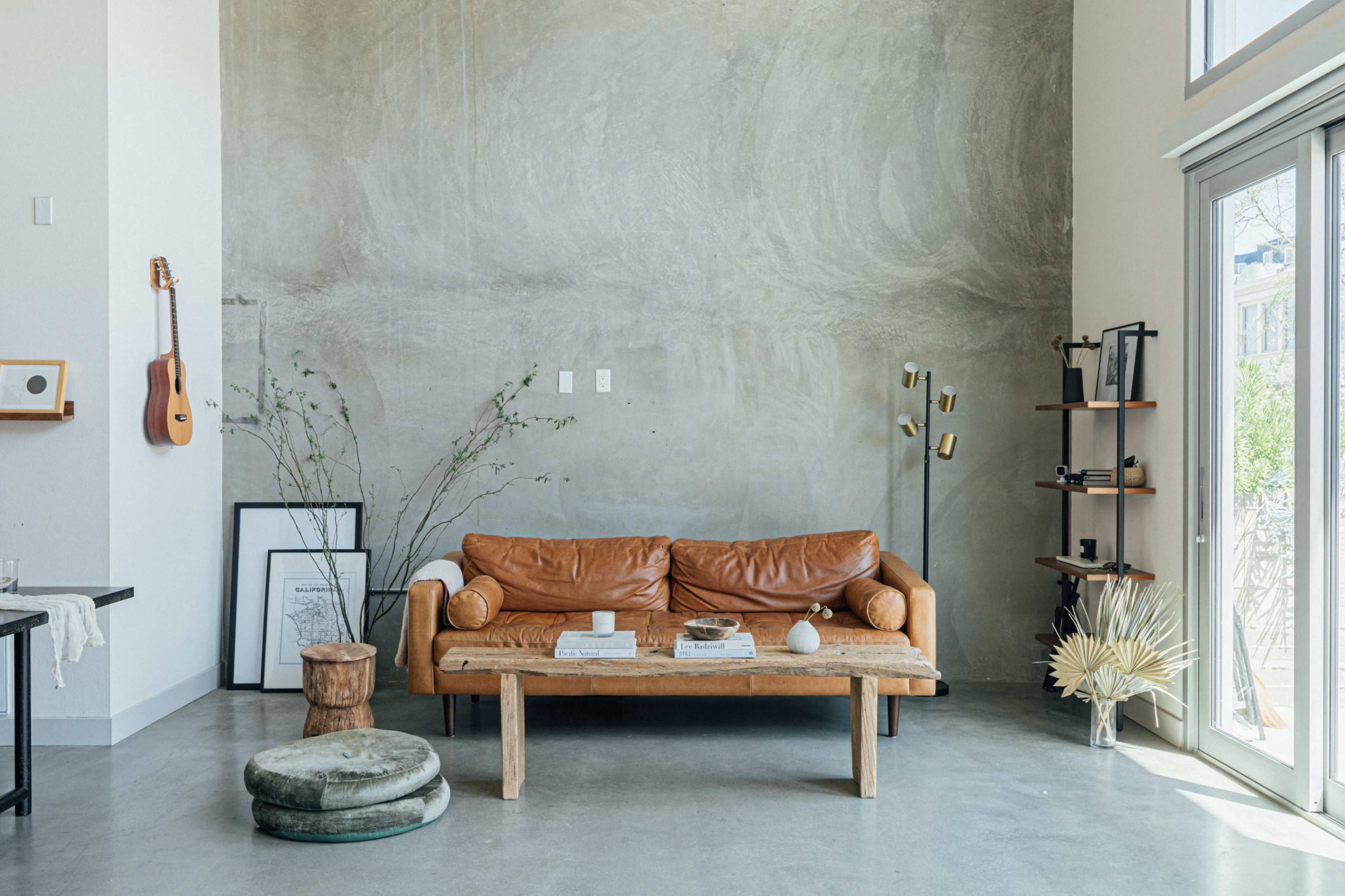 A leather sofa sits against a textured gray wall in a minimalist living room, accompanied by a wooden coffee table and various decorative elements.