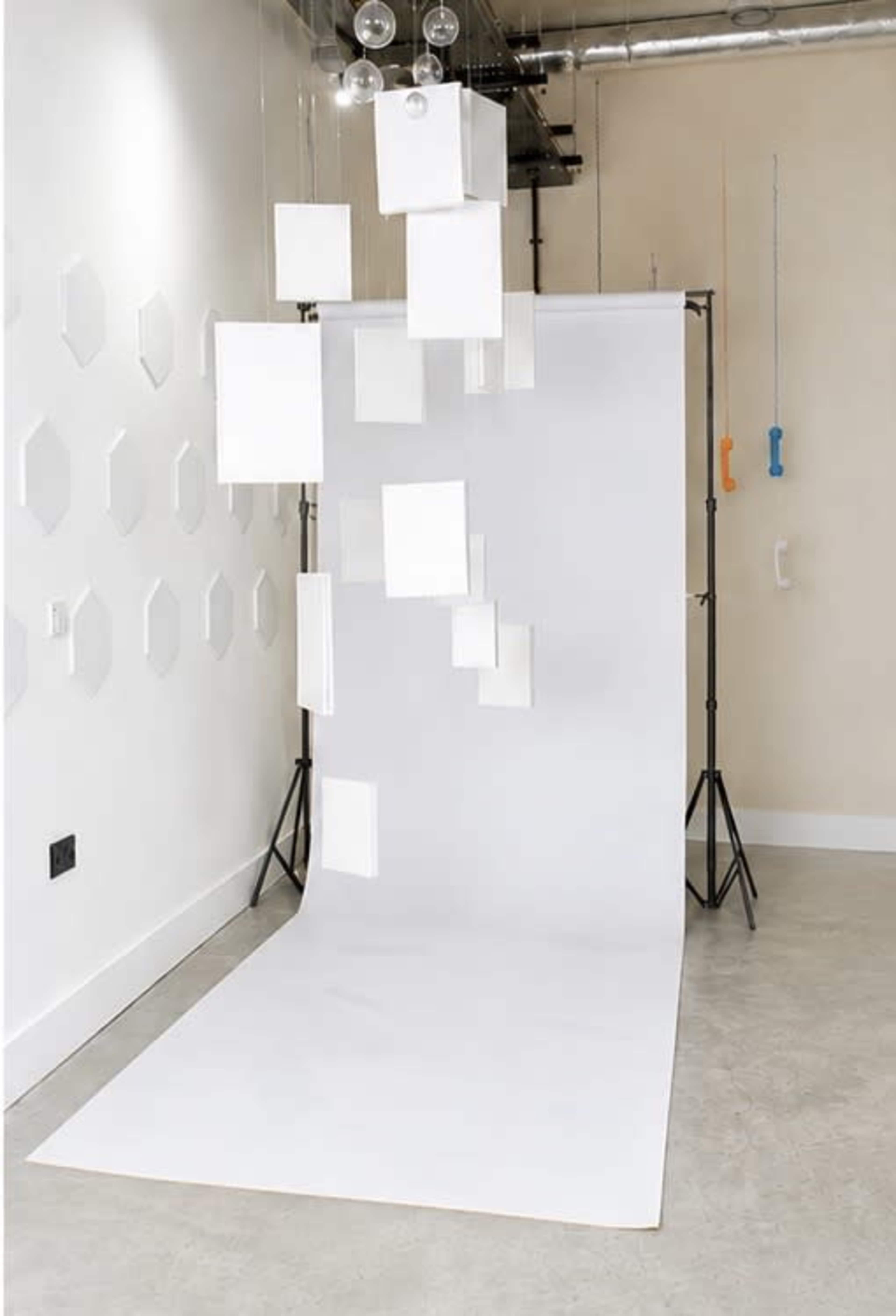 The image shows a simple studio setup with a white backdrop and suspended square panels creating an artistic display.