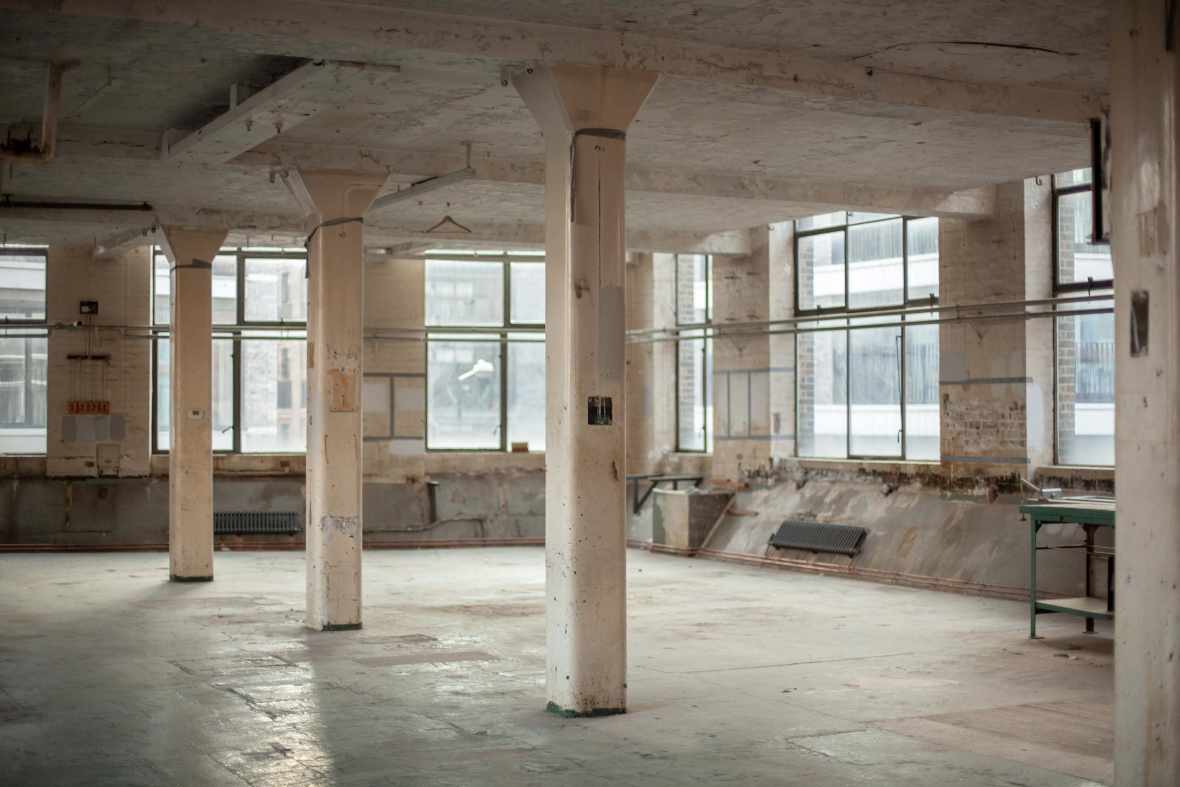 The image shows a spacious, empty industrial room with concrete pillars and large windows.