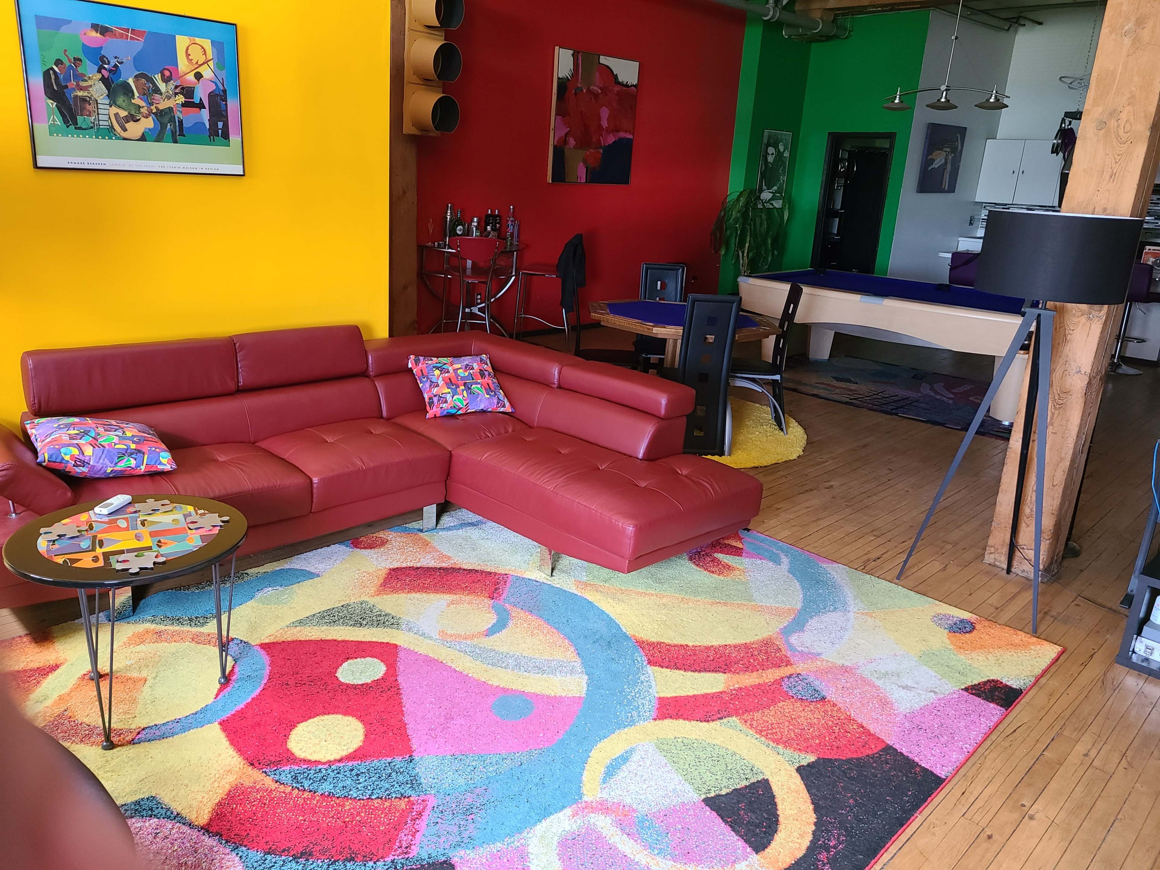 The scene features a vibrant living room with a red sectional sofa, a colorful area rug, and brightly painted yellow and green walls, along with a pool table and modern decor.