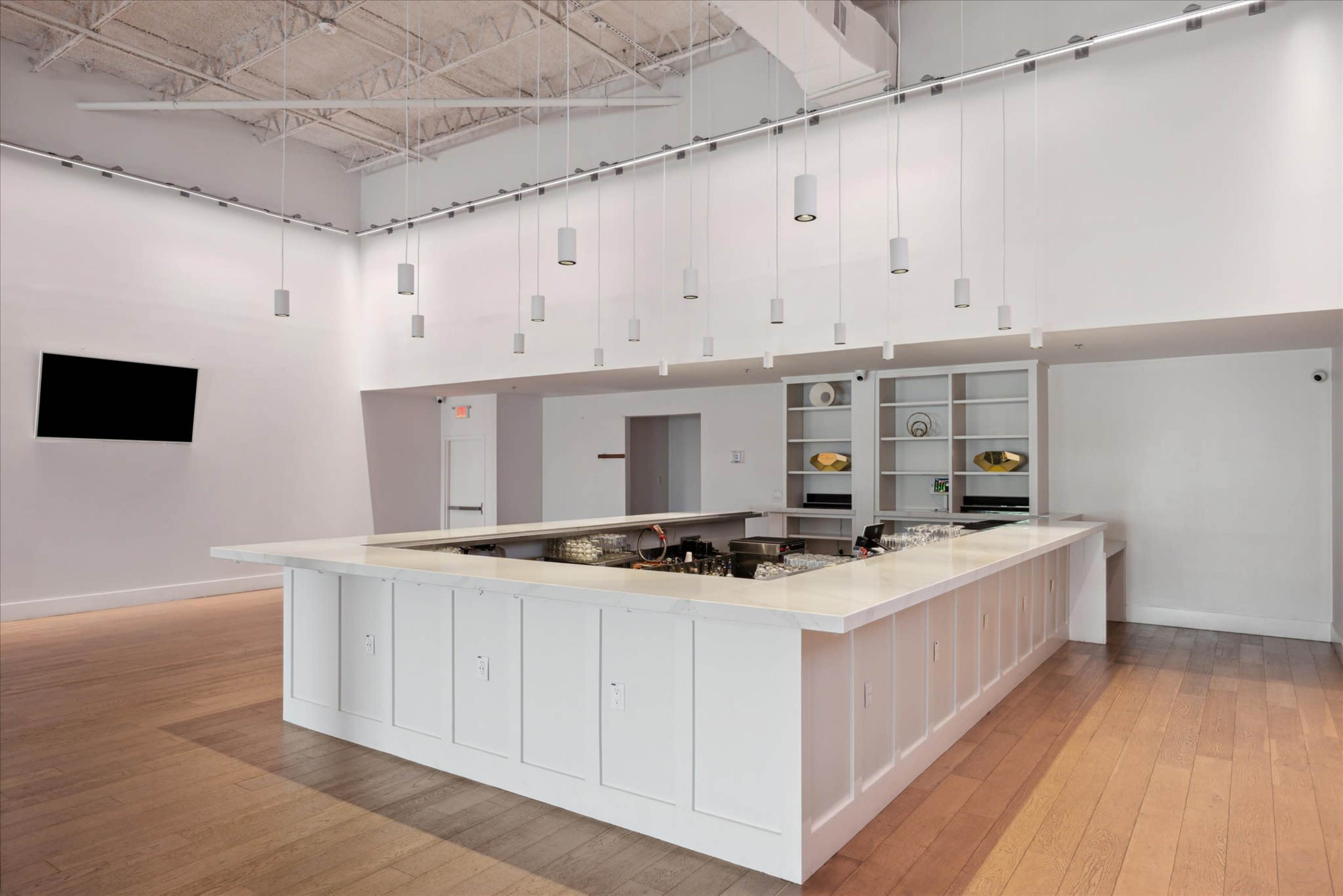 A modern kitchen with a large white island, pendant lights hanging from the ceiling, and a minimalist design.