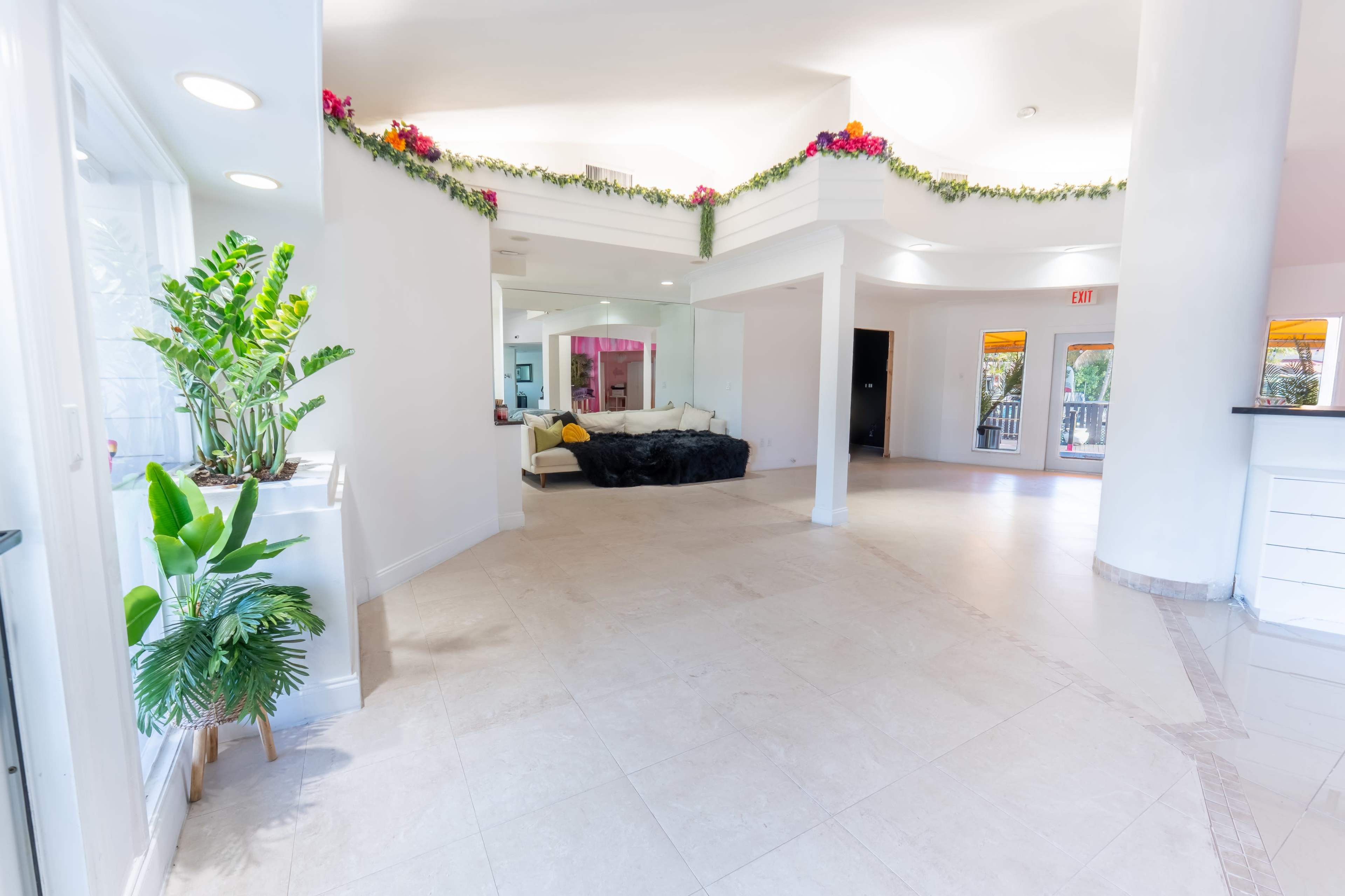 The image shows a spacious, lightly decorated interior with tile flooring, a sectioned living area, and large windows allowing natural light.