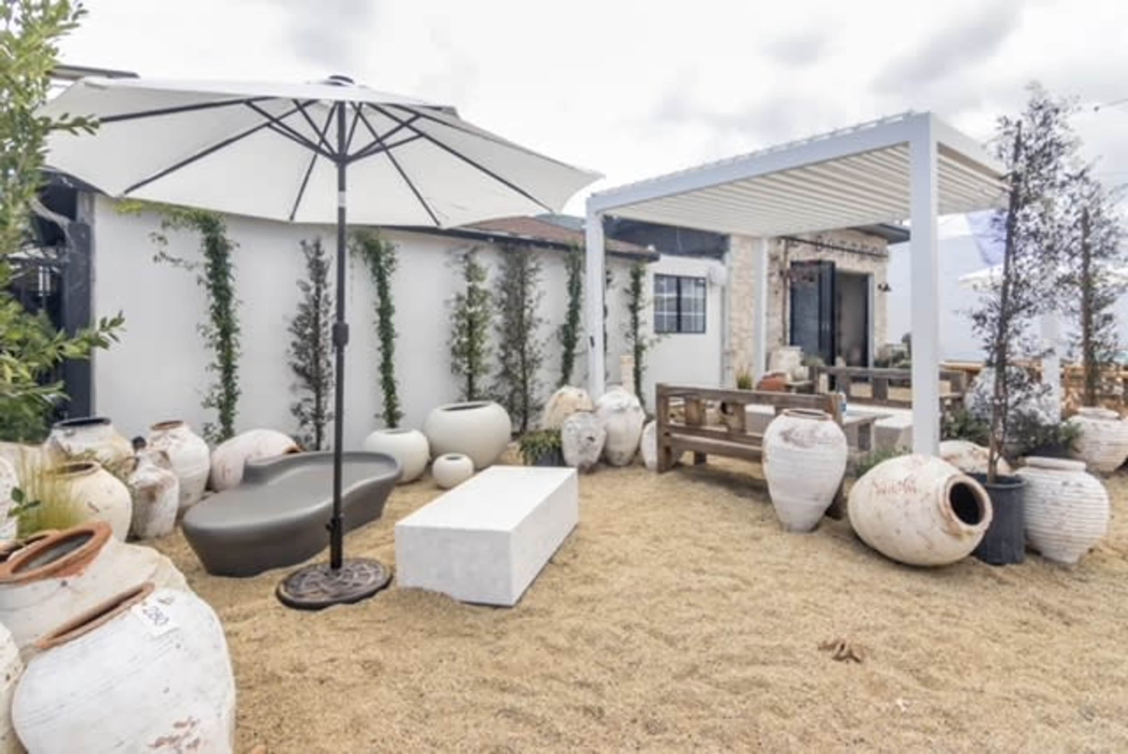 A landscaped outdoor area with various large ceramic jars, a white umbrella, a minimalist bench, and a covered seating area.