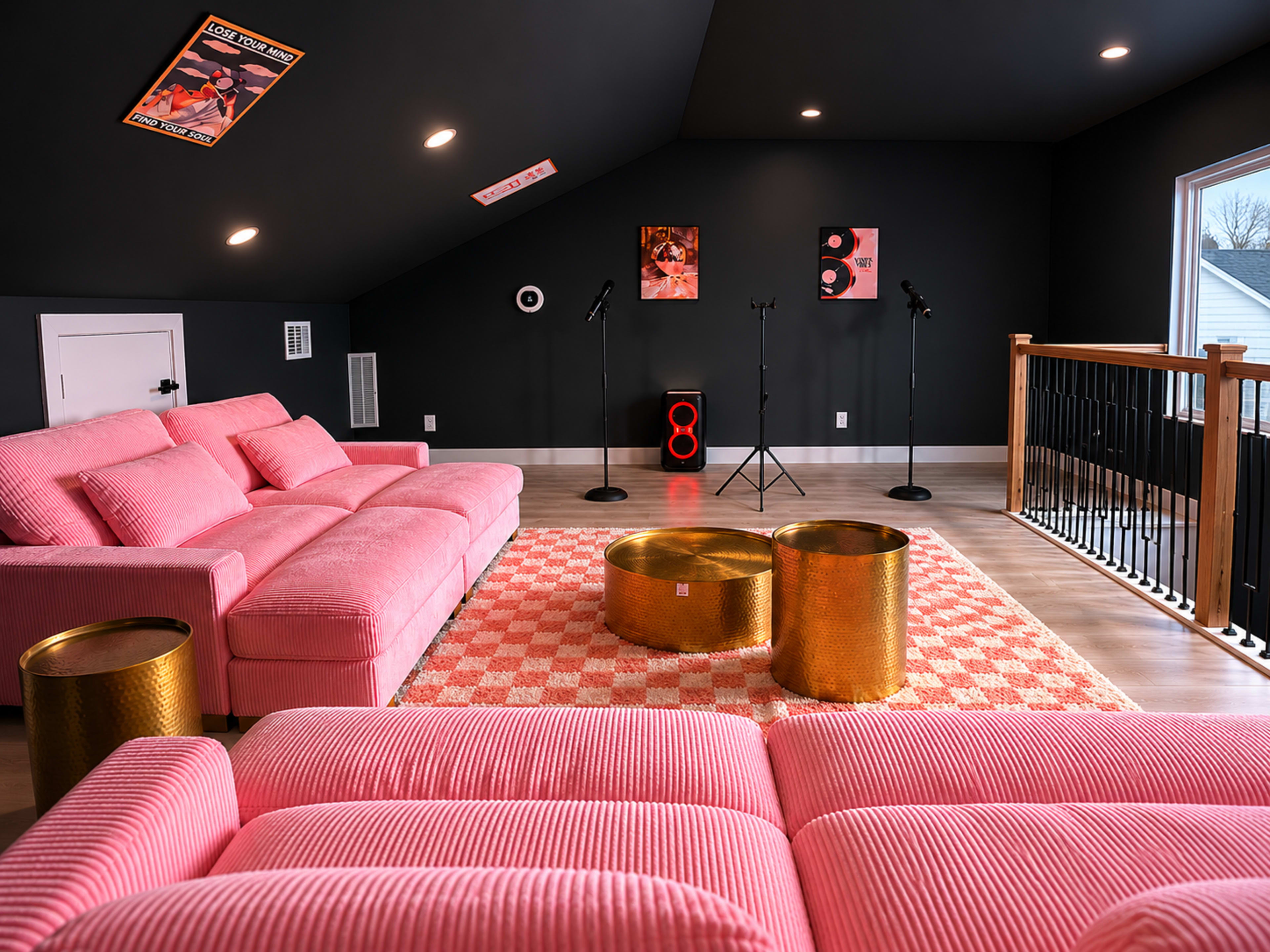 The image shows a modern, stylish lounge room with pink, corduroy sofas, gold accent tables, and a black wall featuring artwork and microphones.