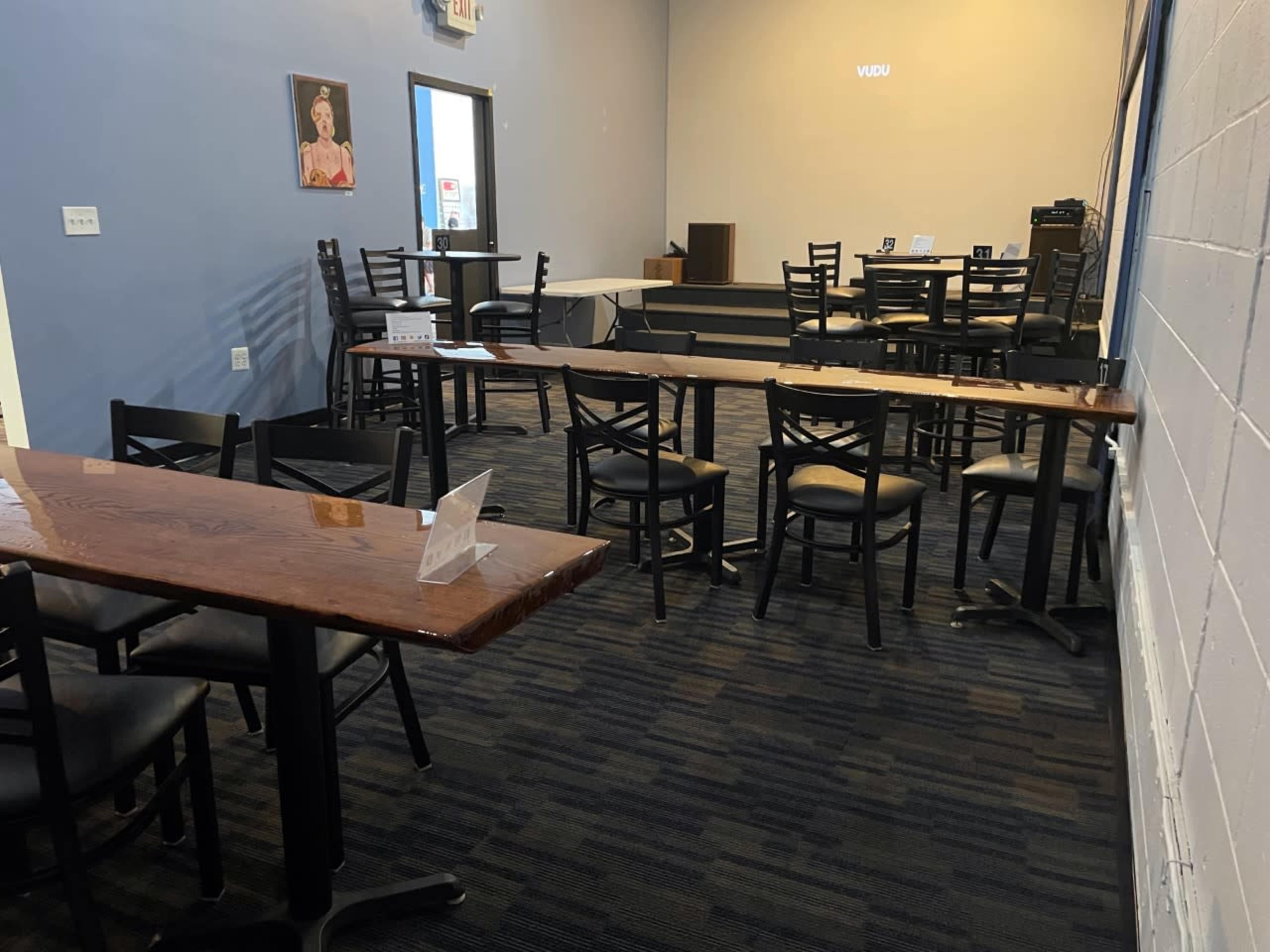 A spacious room with several black chairs and tables, arranged for seating, and a small stage area at the back.