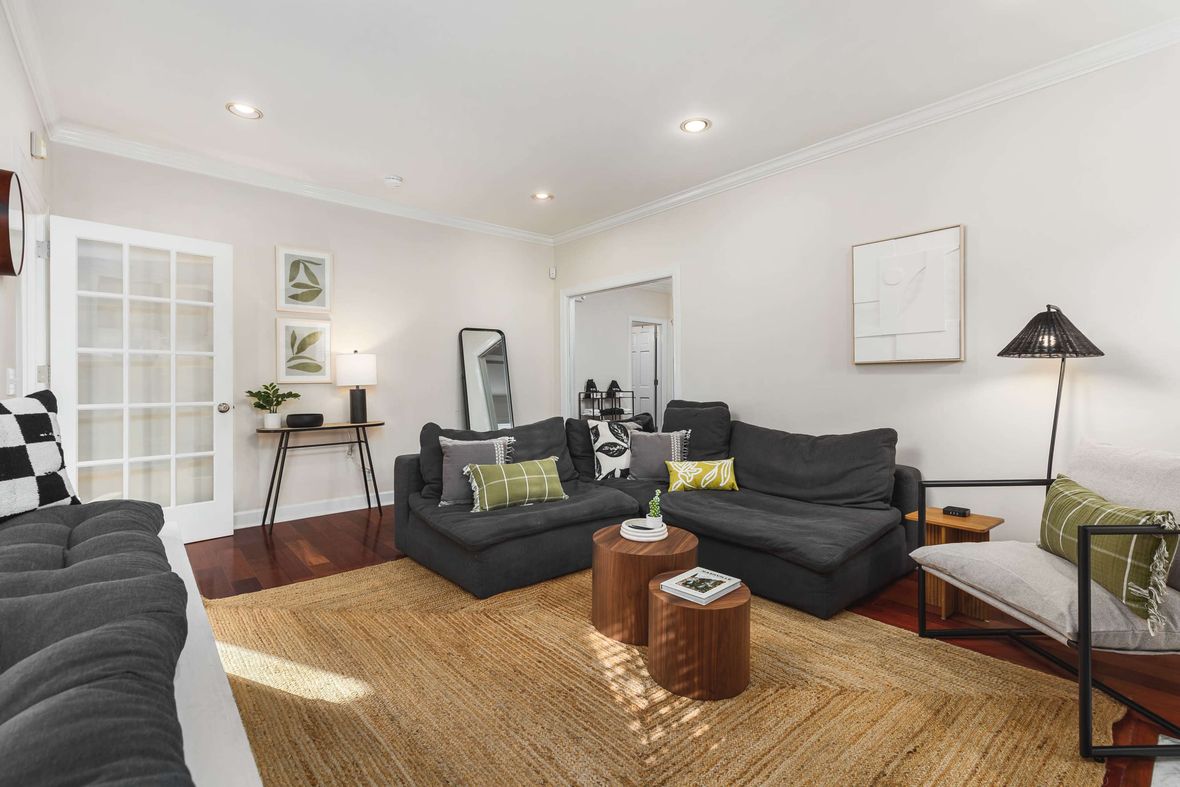 A living room features a dark gray sectional sofa, a light-colored rug, and a small wooden coffee table surrounded by various seating options.