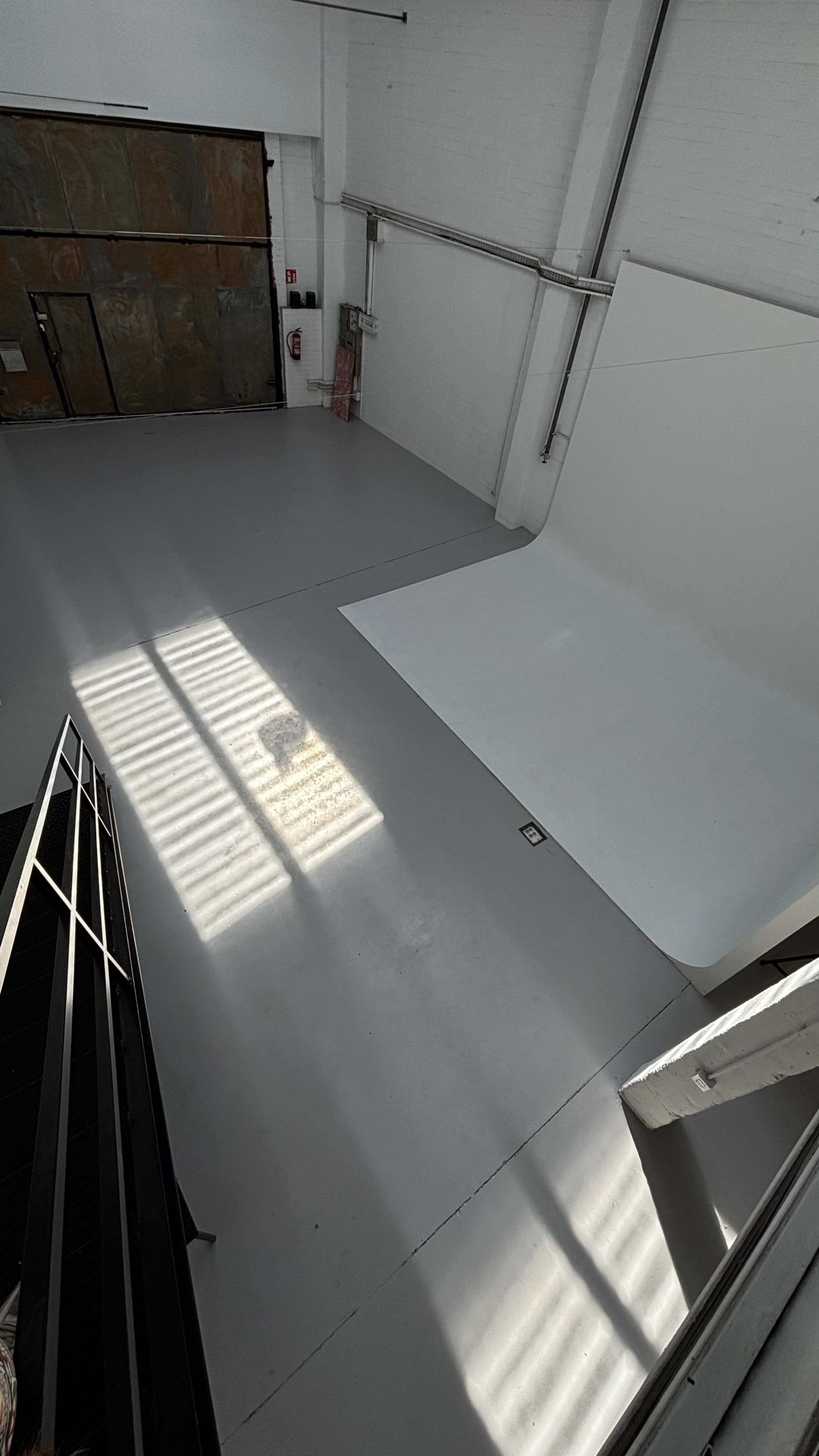 The image shows a spacious studio with a white backdrop and sunlight casting shadows on a gray floor.