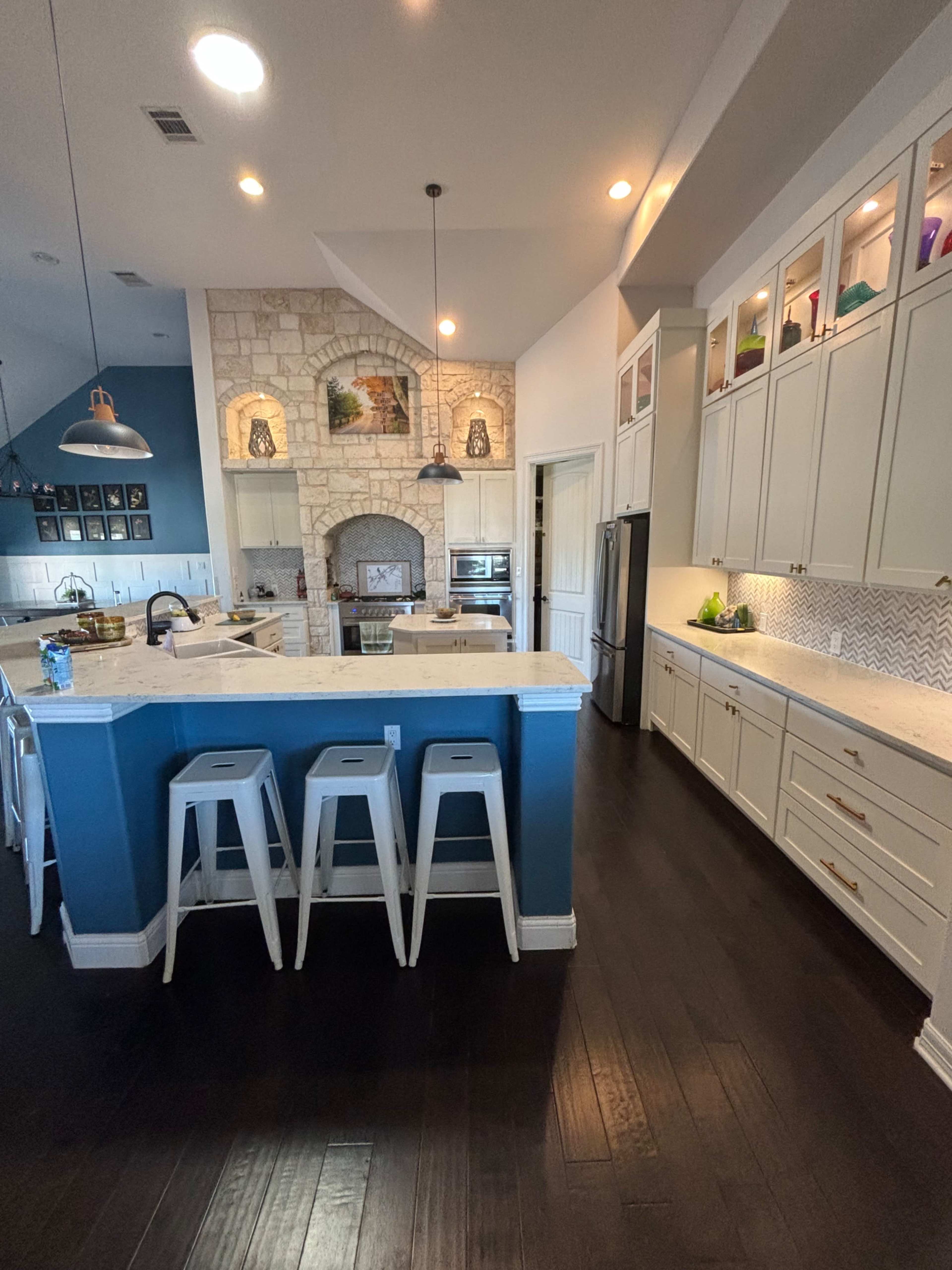 A modern kitchen with white cabinets, a large island with metal stools, and a stone accent wall featuring an archway.