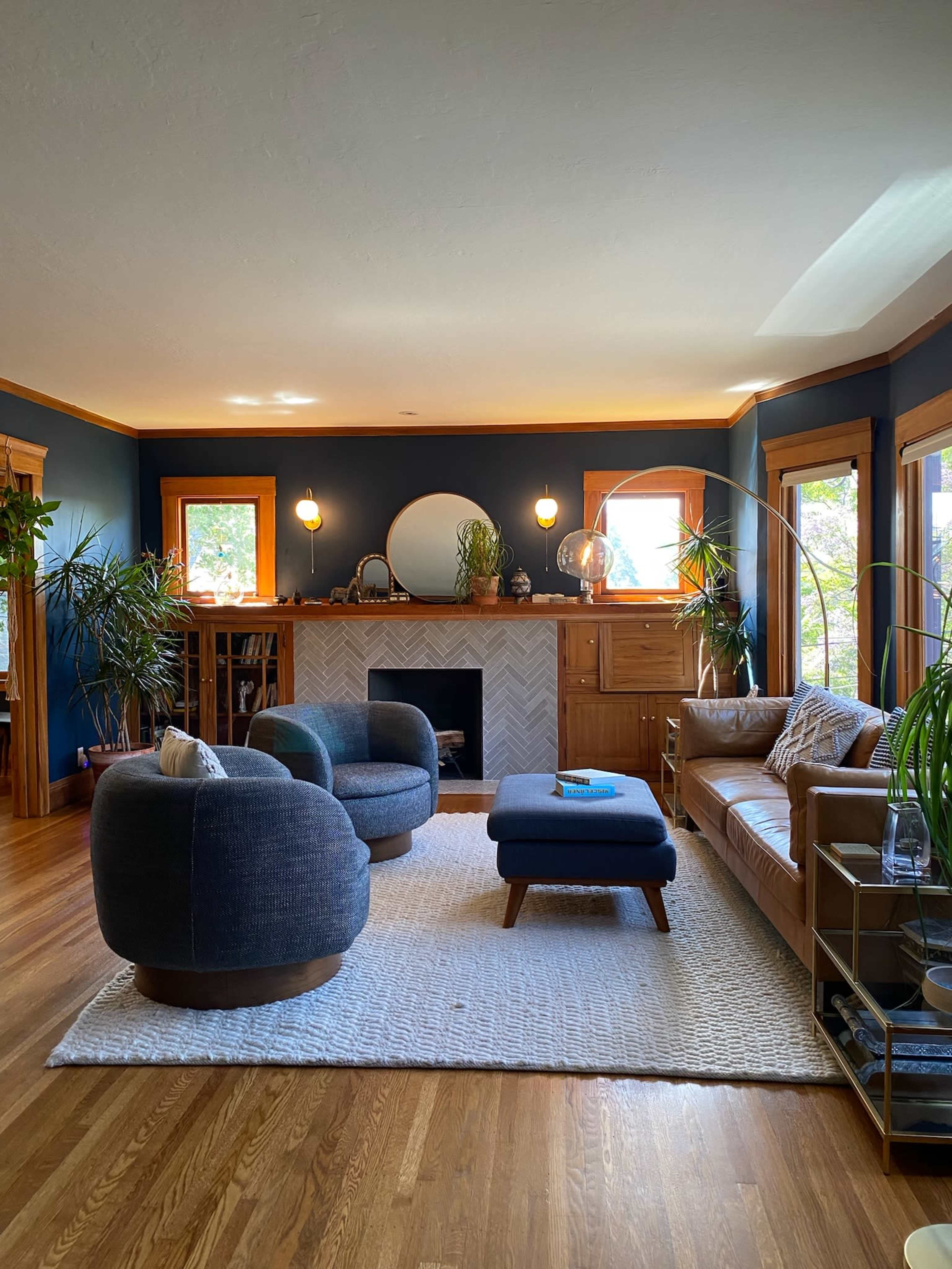A cozy living room features a mix of plush seating, a fireplace with a herringbone design, and large windows allowing natural light.