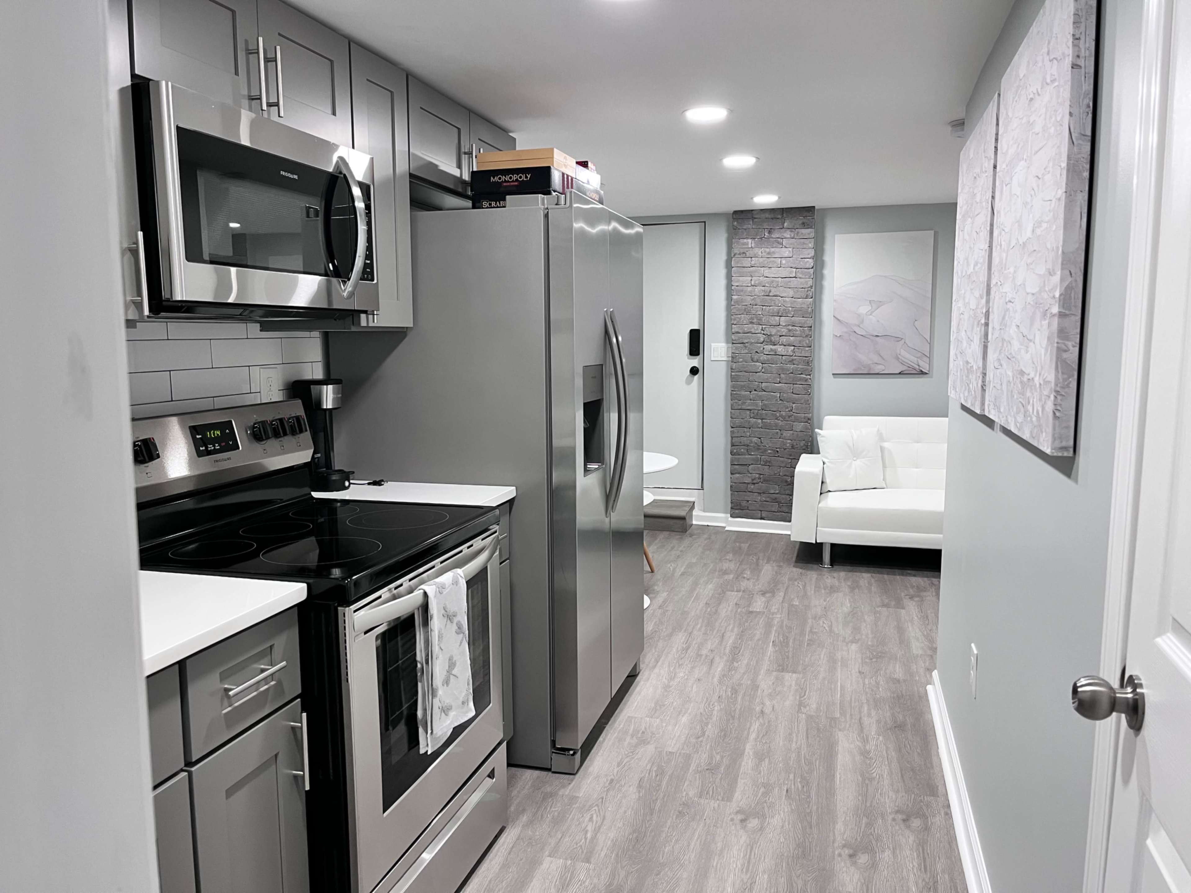 A modern kitchen with stainless steel appliances, including a microwave and refrigerator, adjacent to a small living area with a white couch.