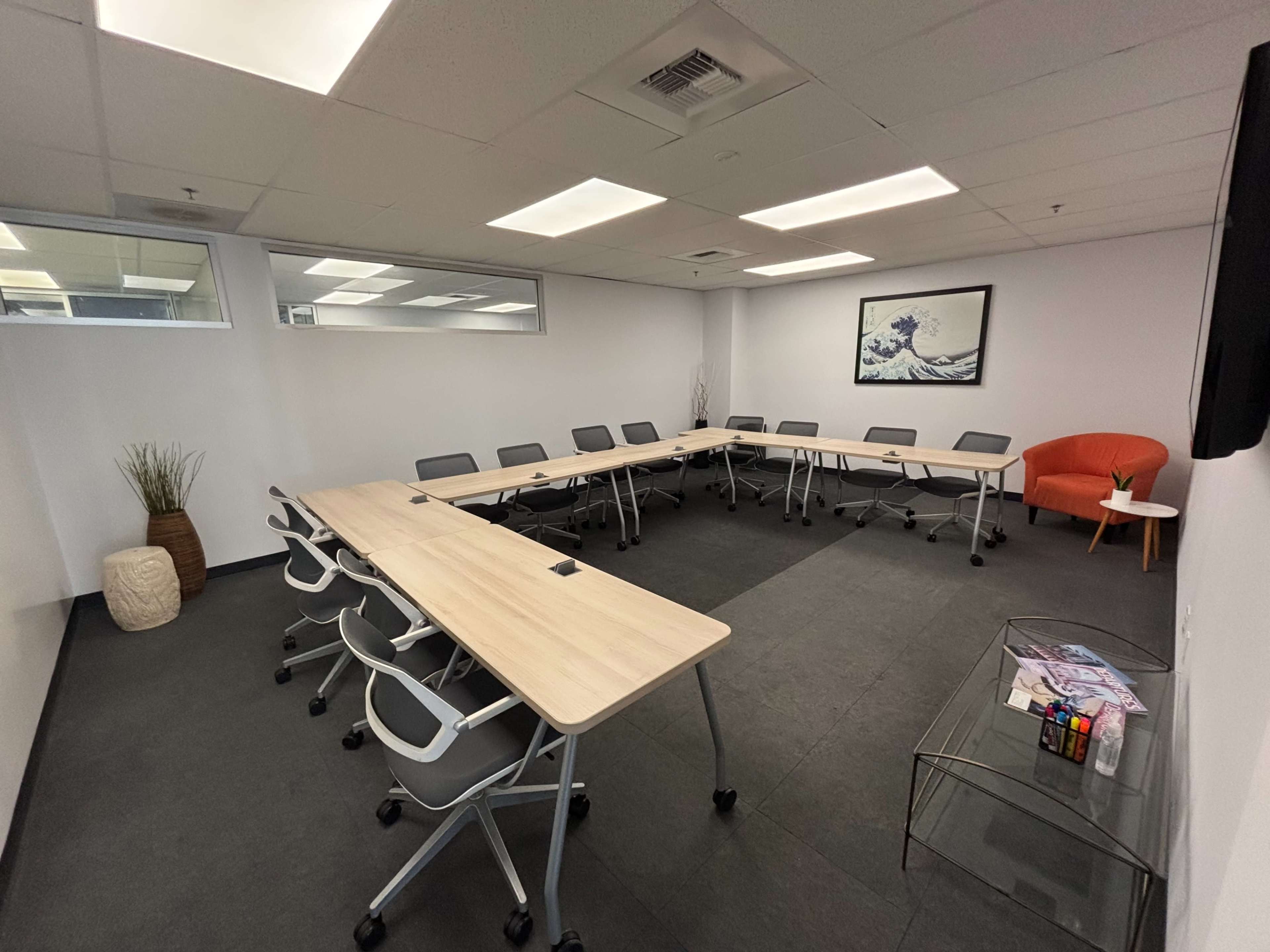 The image shows a modern conference room arranged with multiple tables and chairs, featuring a minimalist design and a large wall art piece.
