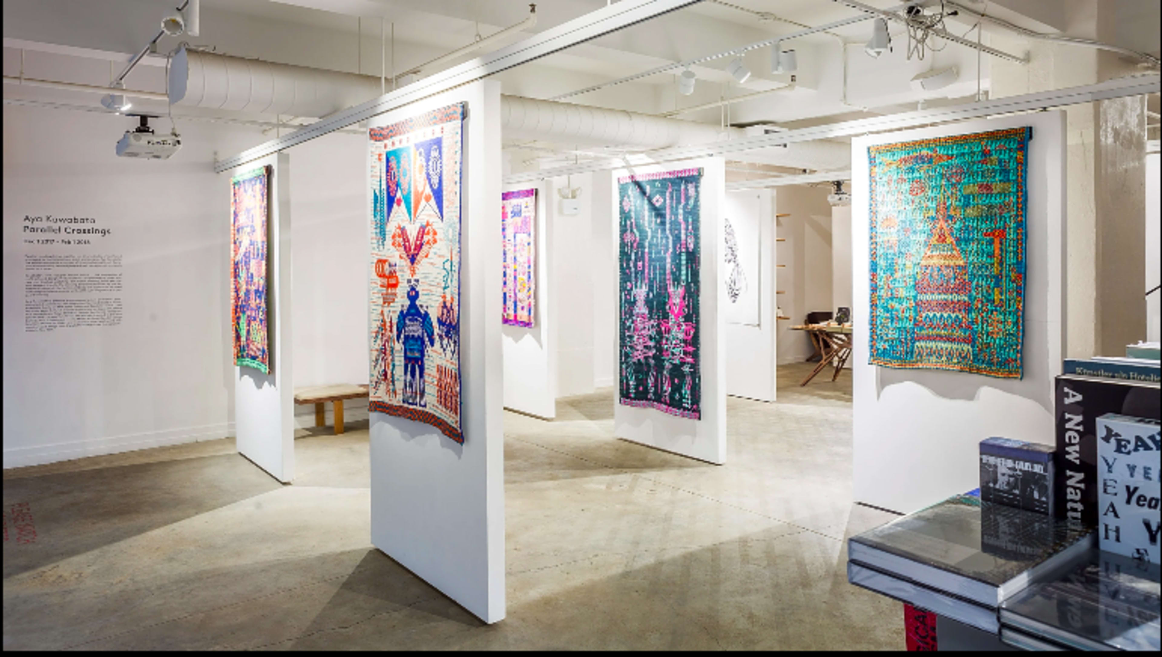 An art exhibition with colorful tapestries displayed on white walls in a spacious gallery.