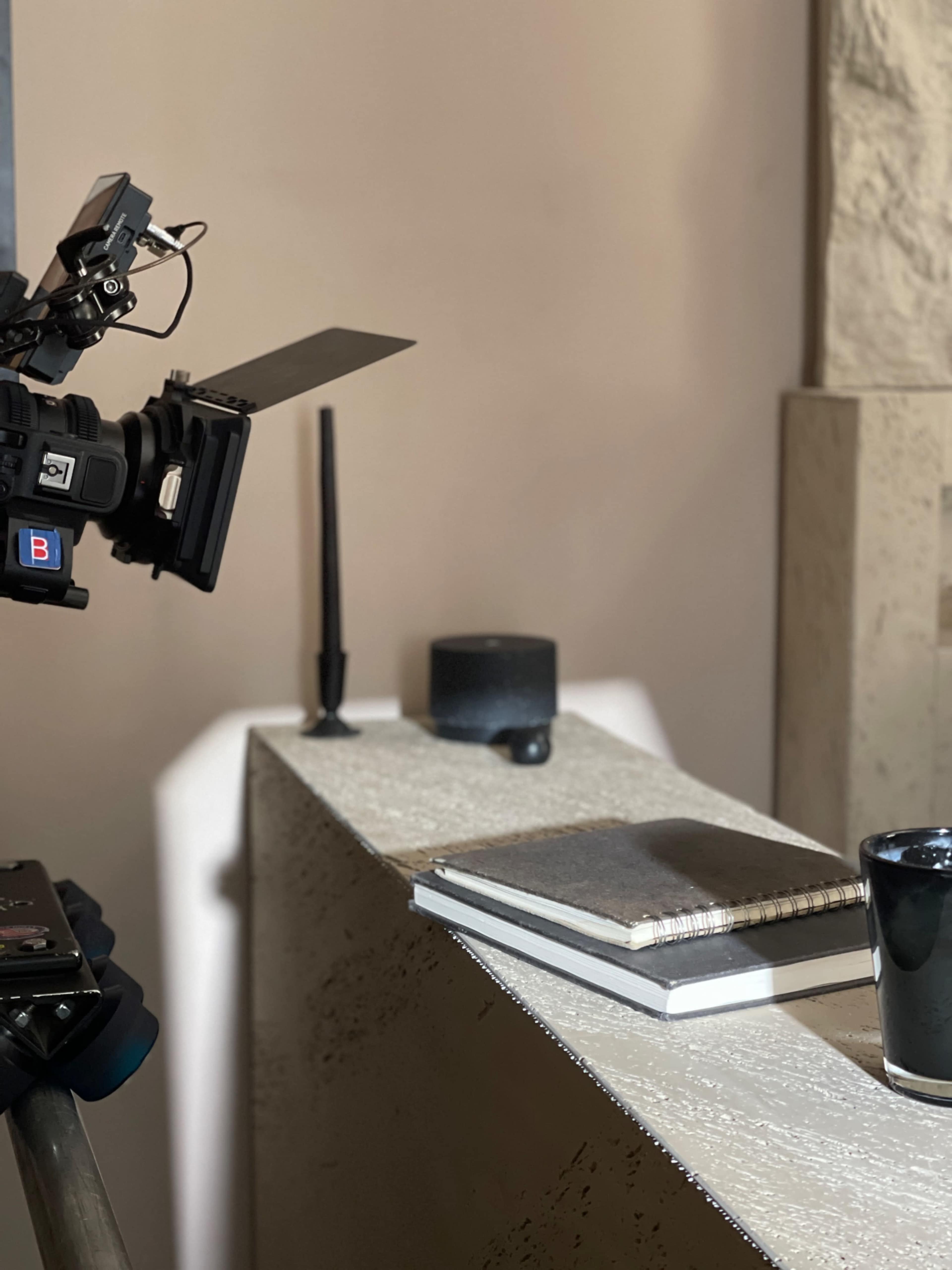 A camera is positioned near a concrete surface featuring a notebook and a cup.