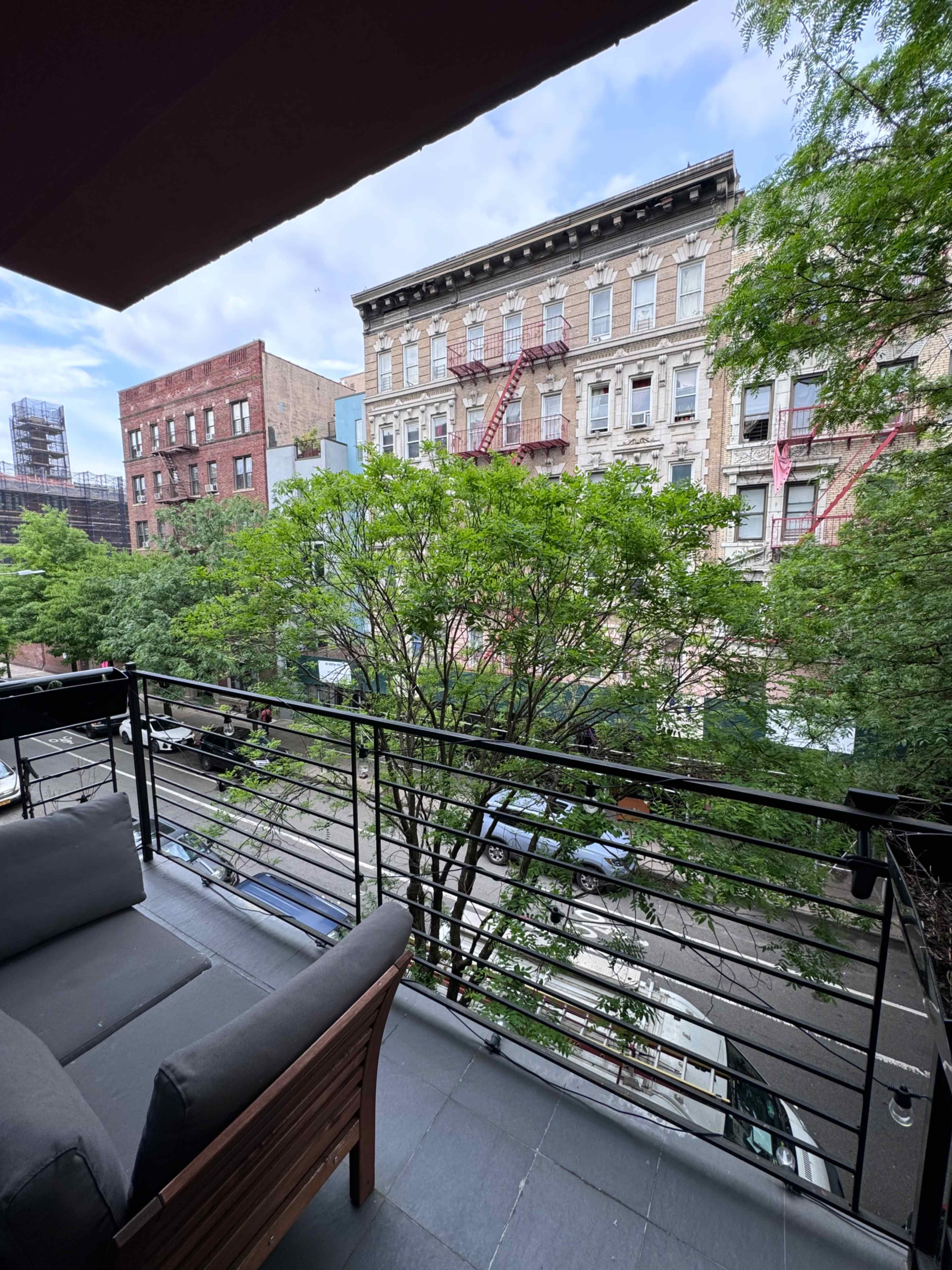 A balcony view overlooking a tree-lined street with a mix of brick buildings and parked vehicles.