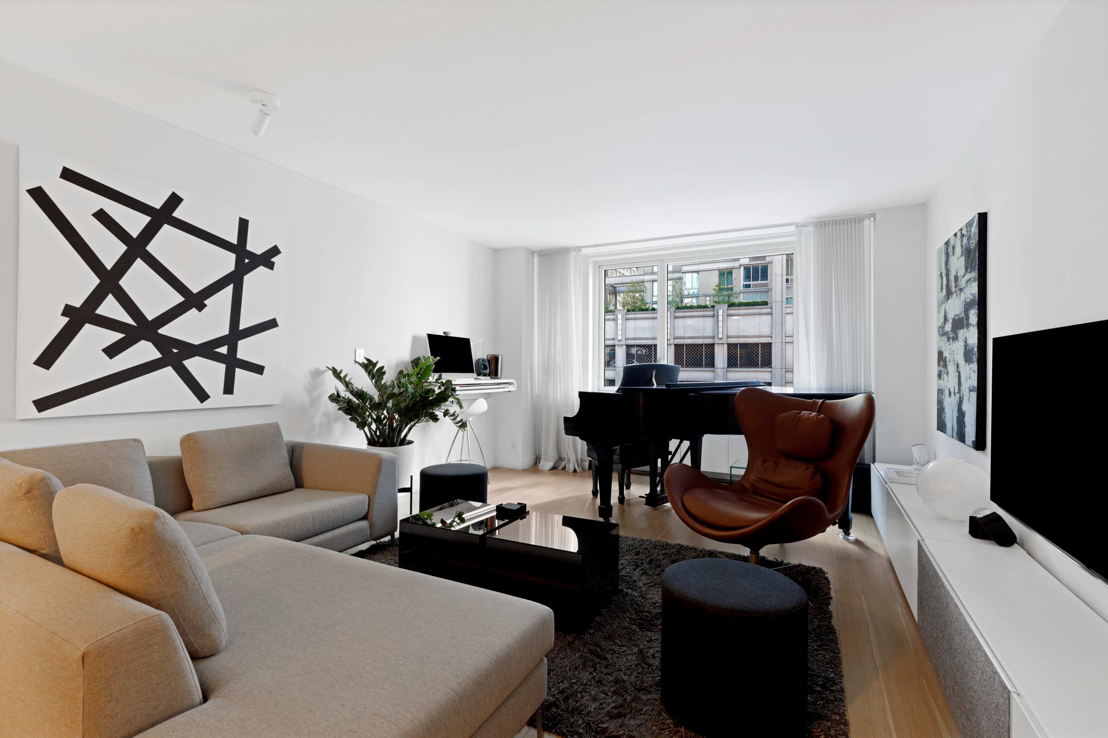 A modern living room features a gray sectional sofa, a black coffee table, a piano, and abstract artwork on the walls.