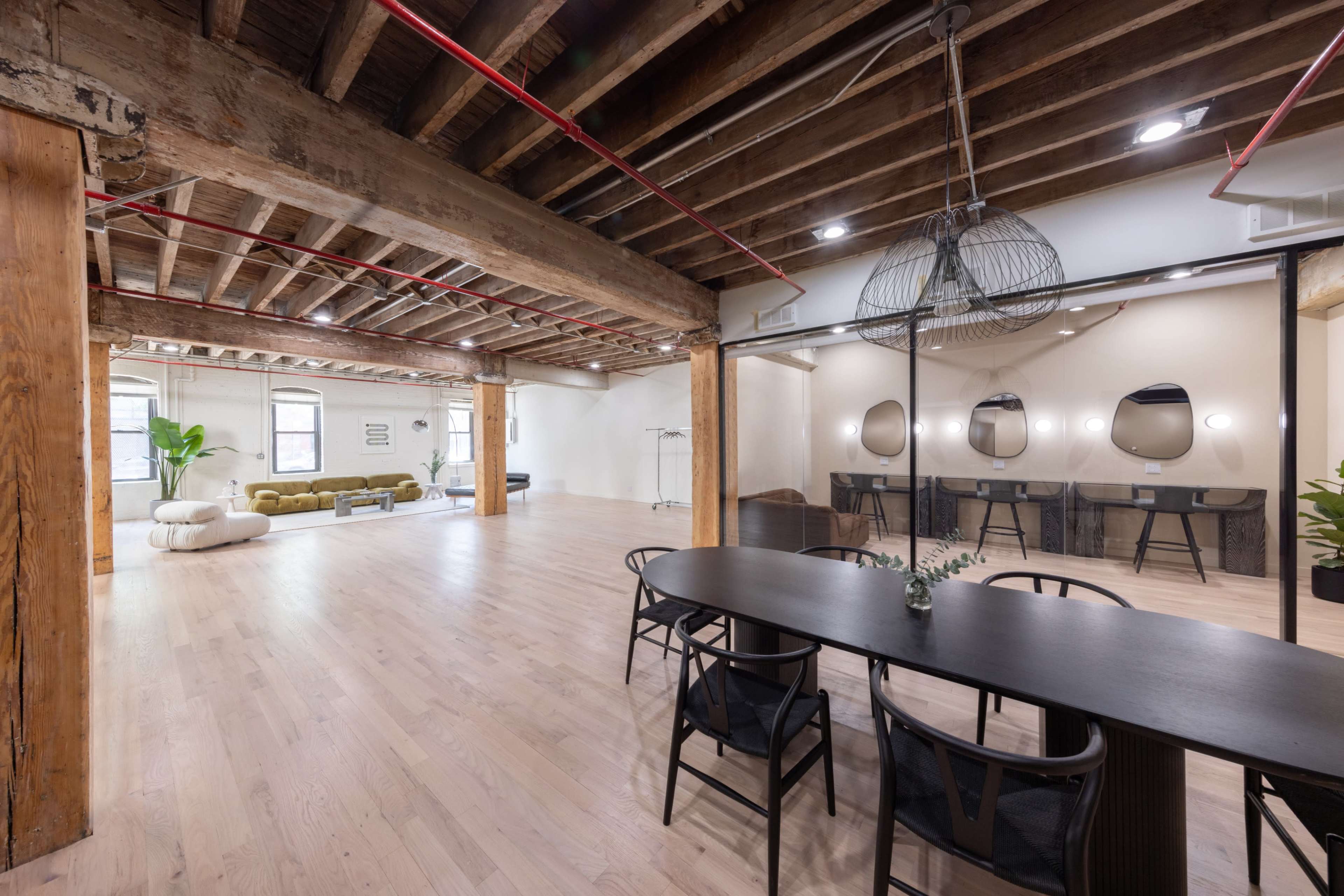 A spacious interior with wooden beams, a long black dining table, and a mix of lounge and work areas featuring modern furniture.