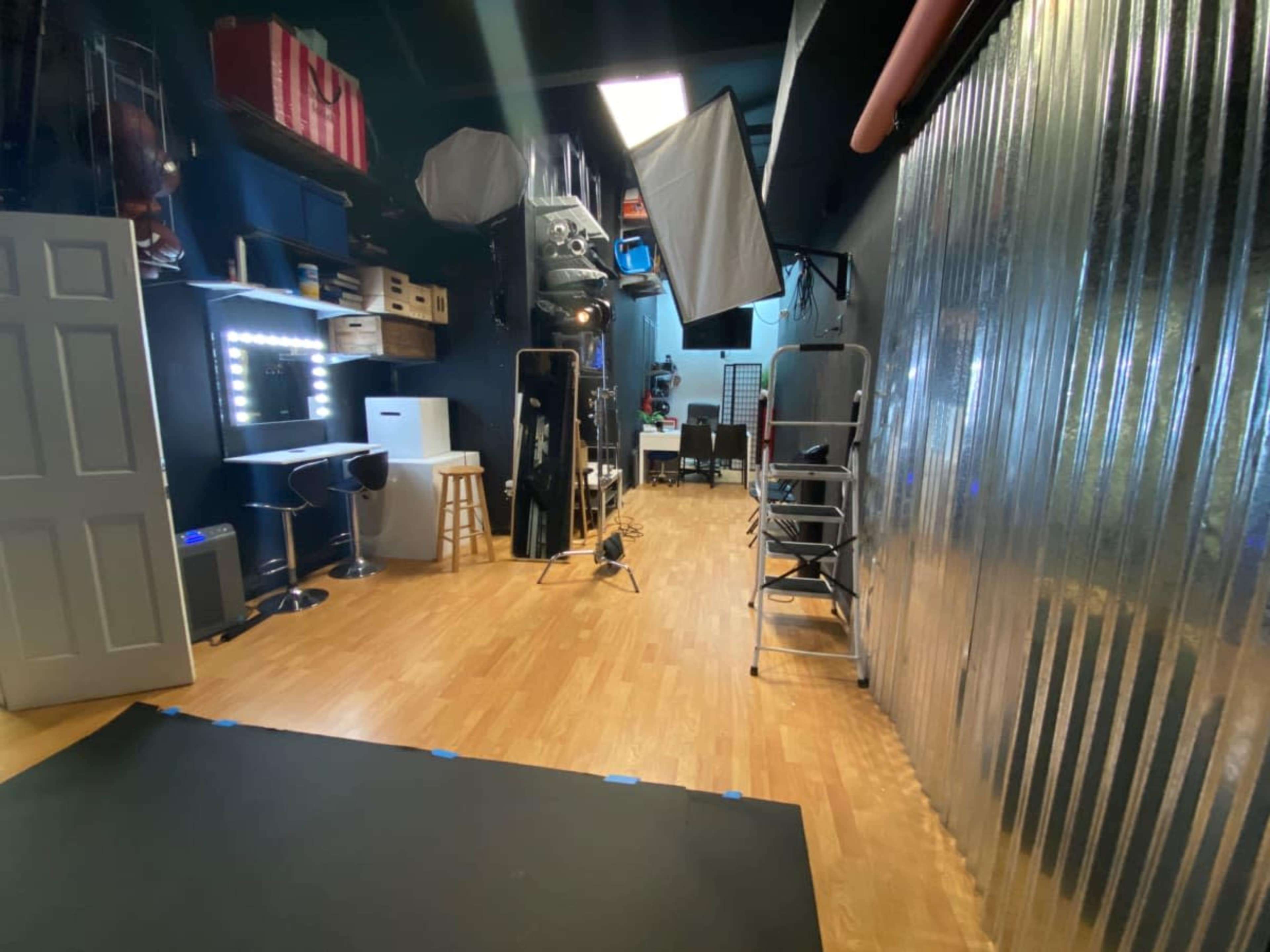 The image shows a well-lit photography studio featuring a wooden floor, various equipment, and a makeup station with a large mirror.