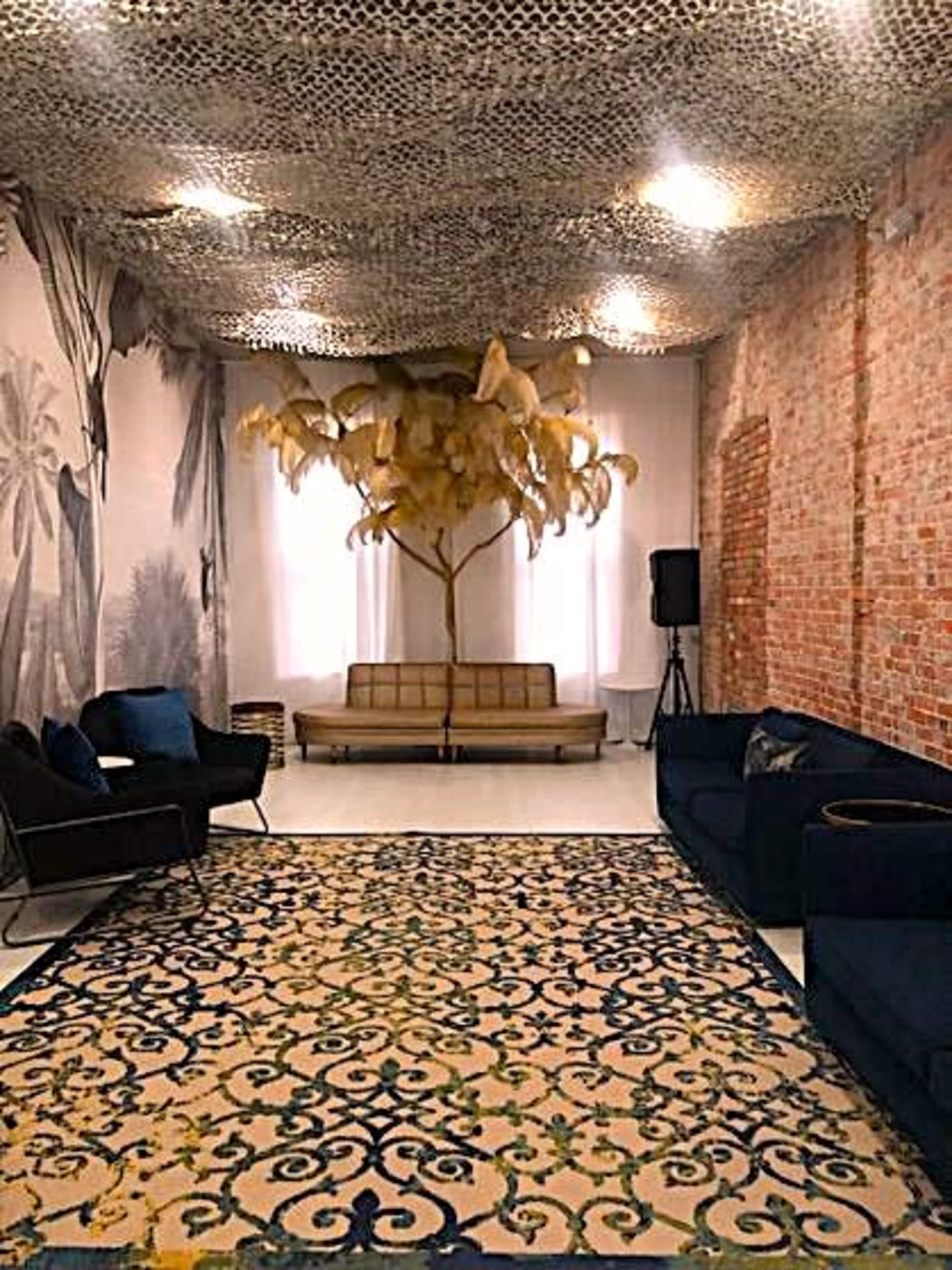 A stylish lounge area featuring a patterned rug, a vintage couch, and a decorative tree installation beneath a textured ceiling.