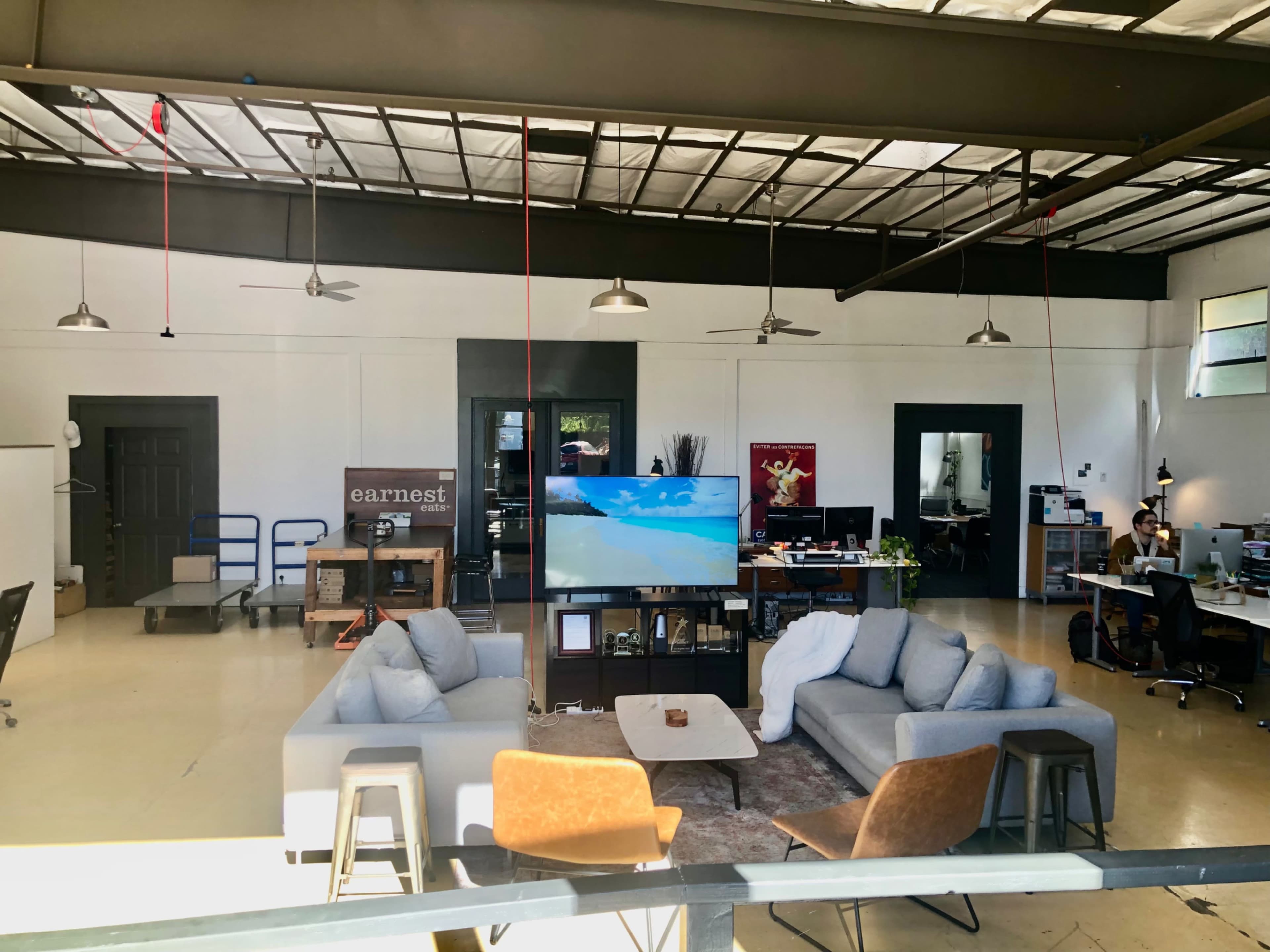 An open office space featuring a lounge area with sofas, a television, and workstations equipped with computers.