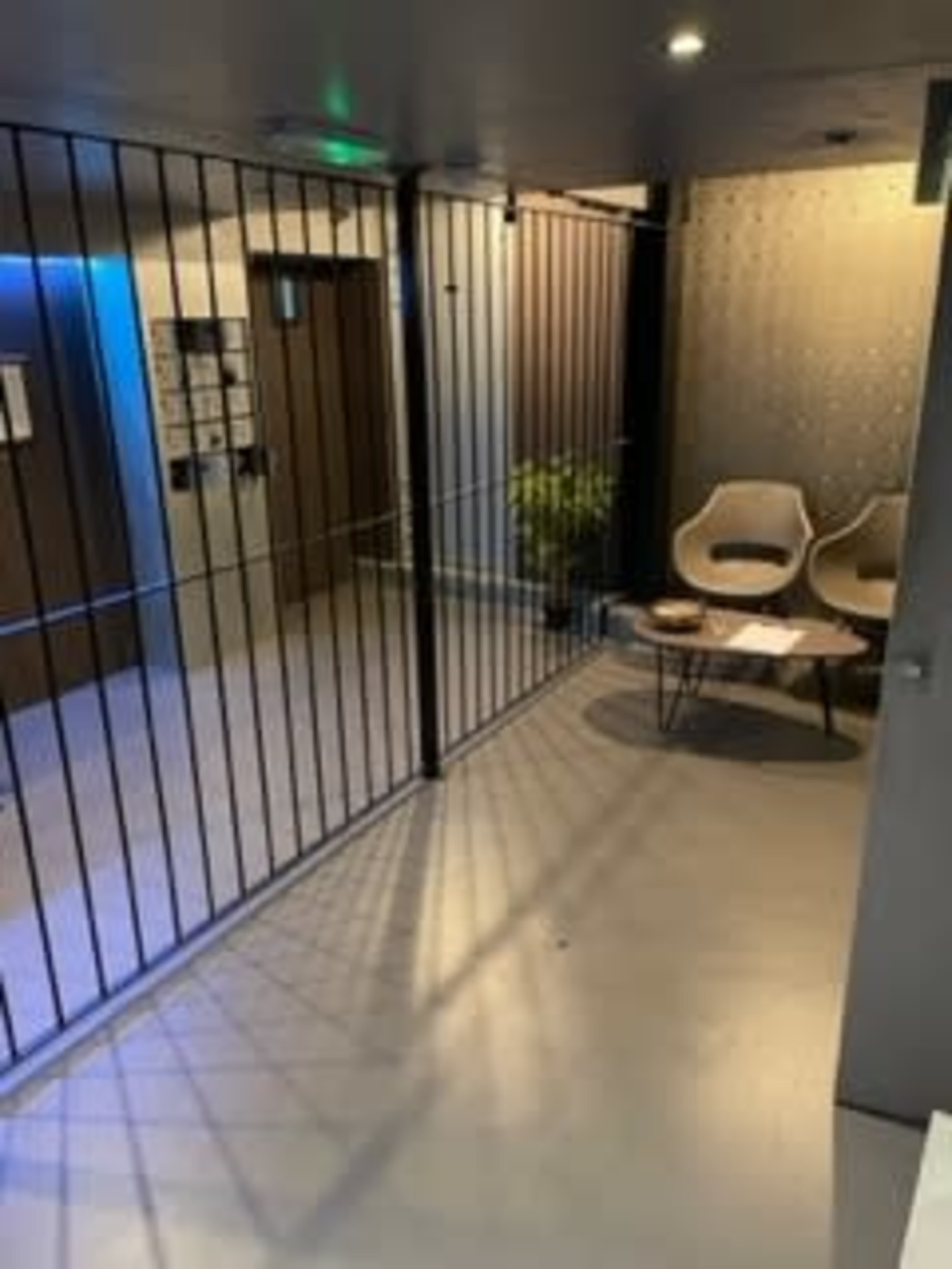 A corridor with metal bars dividing a seating area from an elevator access point, featuring two chairs and a small table.