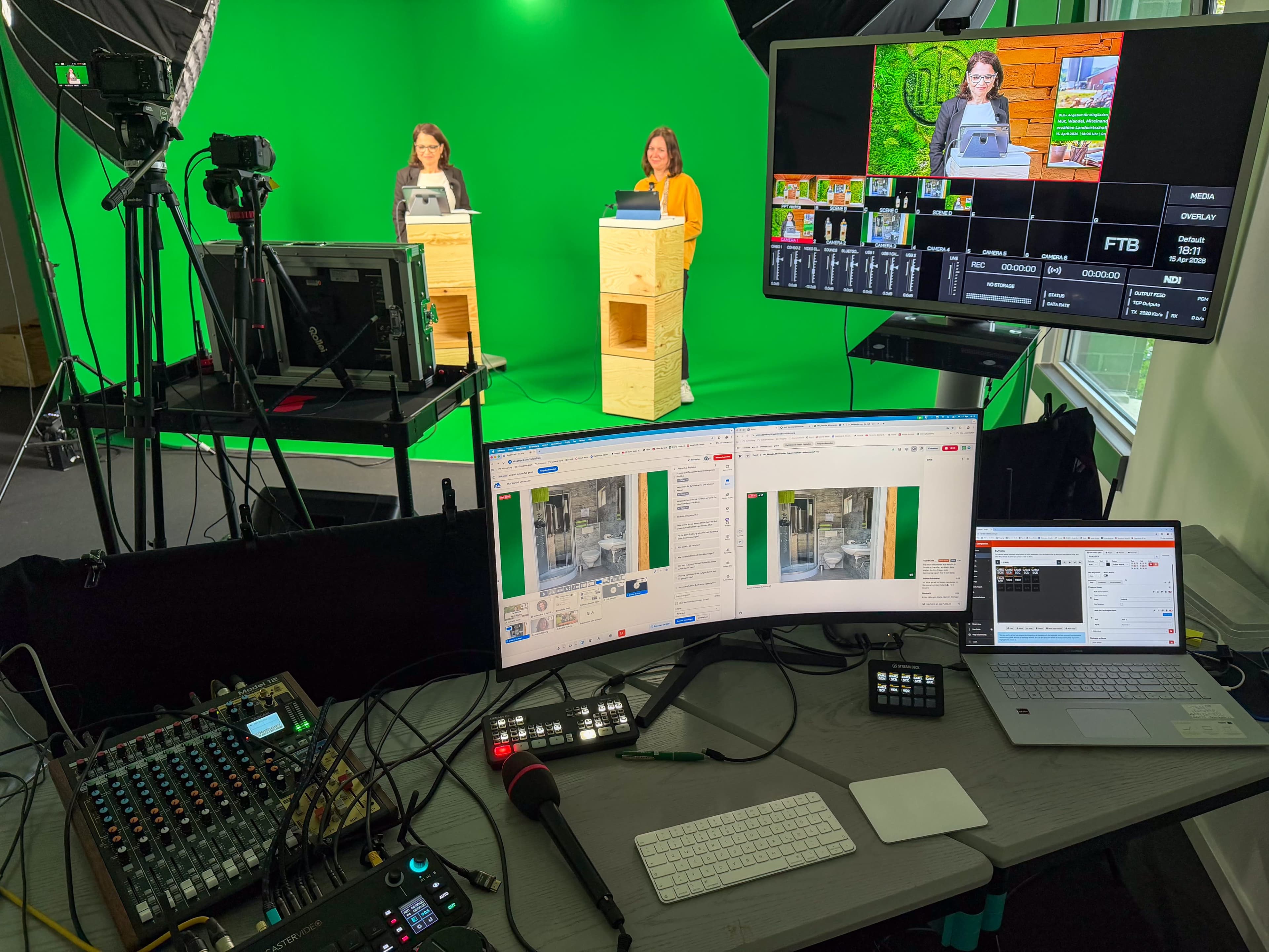Two women present in front of a green screen while surrounded by recording equipment and monitors displaying broadcast controls.